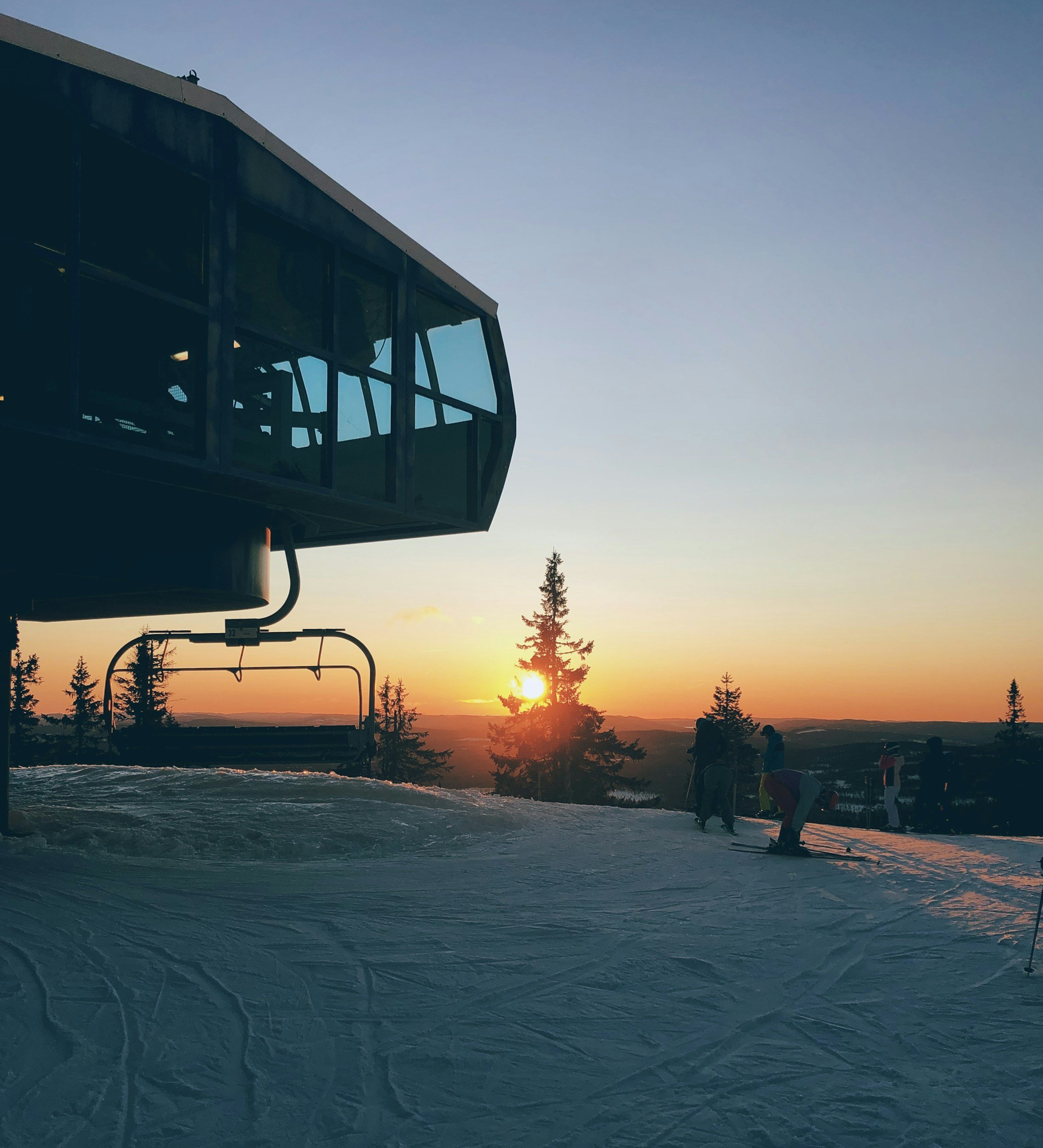 Sunset at Trysil alpine ski resort in winter, showing ski lifts, groomed slopes and forested mountain landscape.