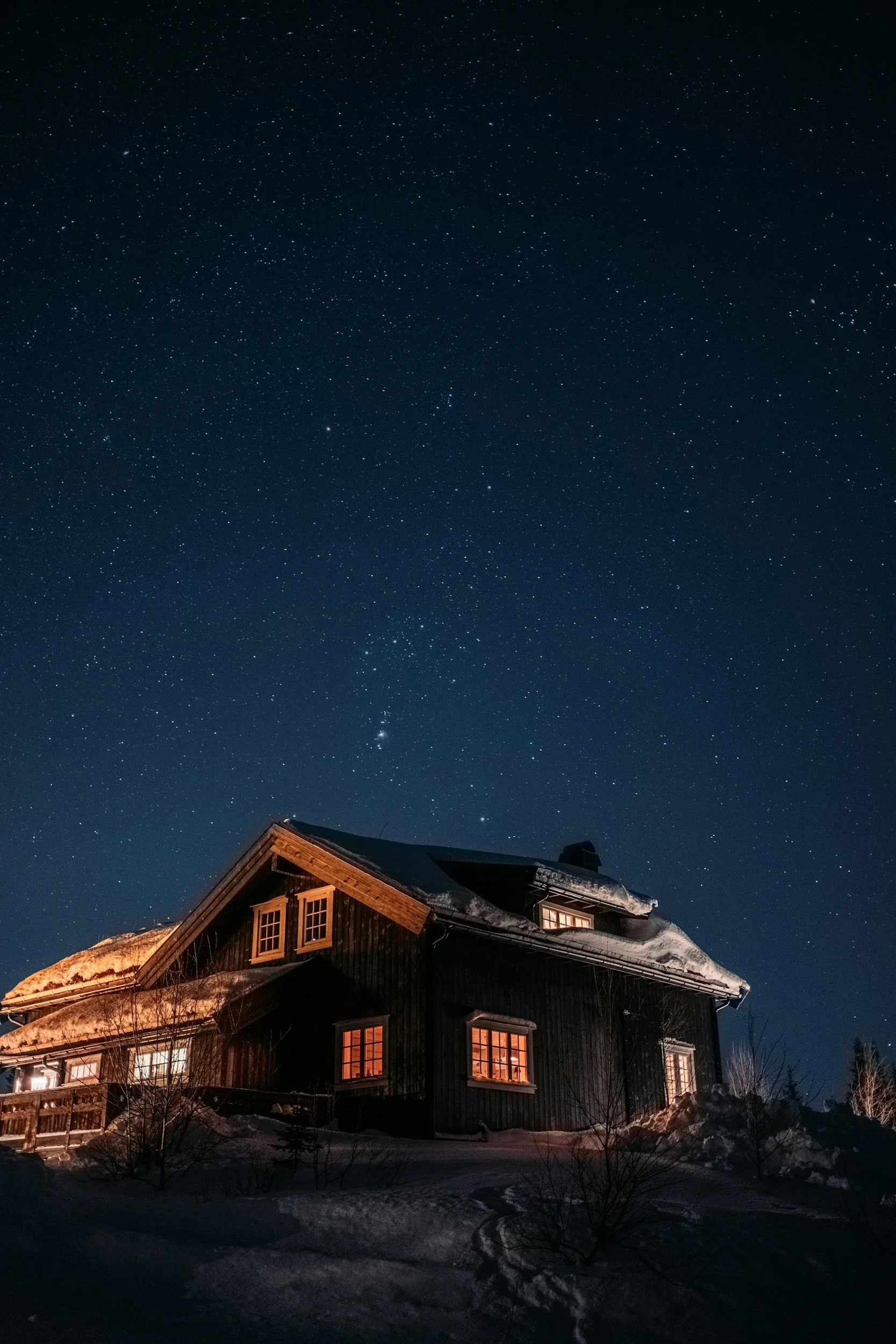 Mountain cabin in Hafjell at night in winter, with warm lights glowing from windows and snow-covered surroundings.