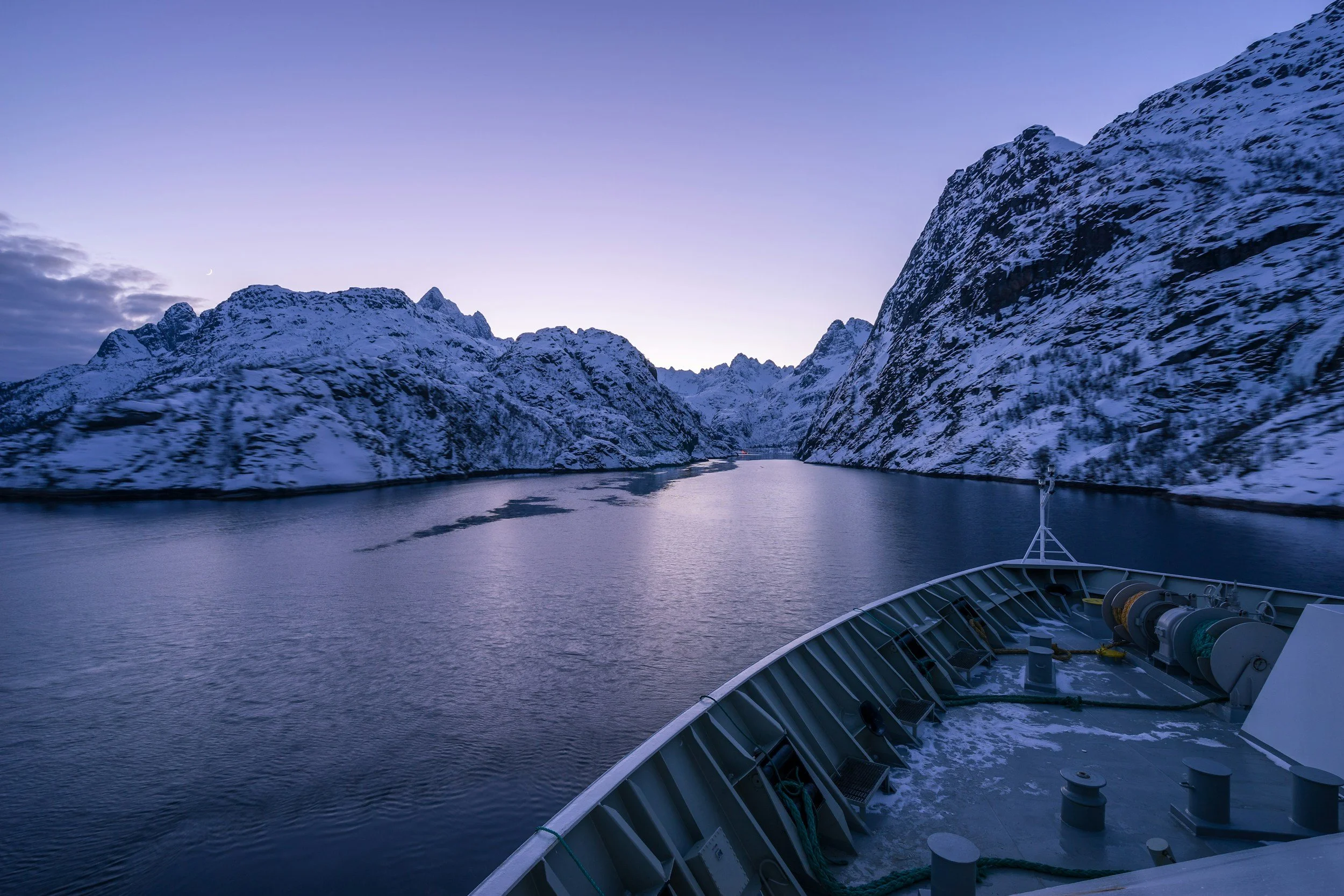The front of the hurtigruten ship looking towards the snow covered mountains at sunset.