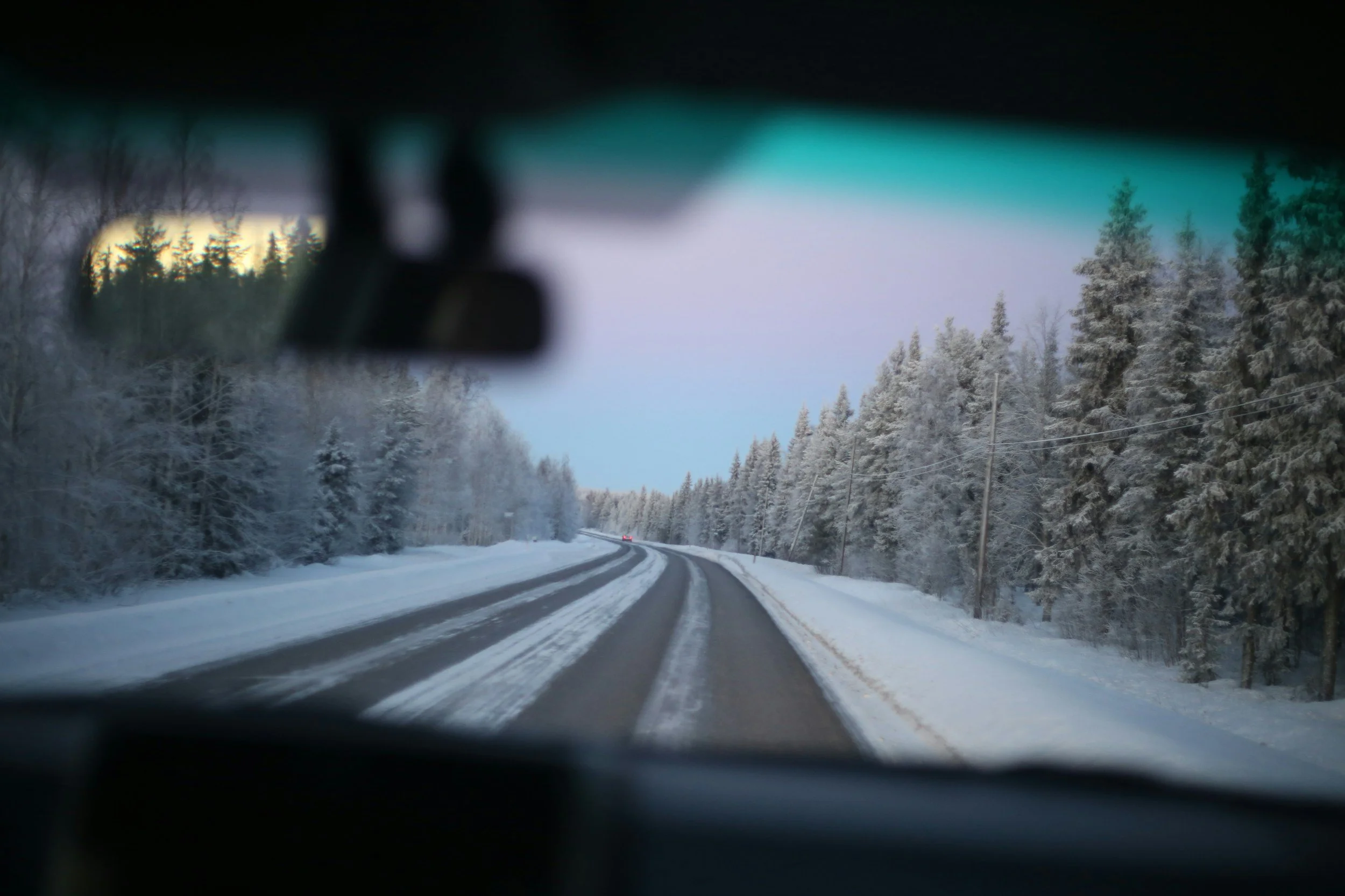 Winter road in Norway viewed from inside a car, with snow-covered trees and icy driving conditions.