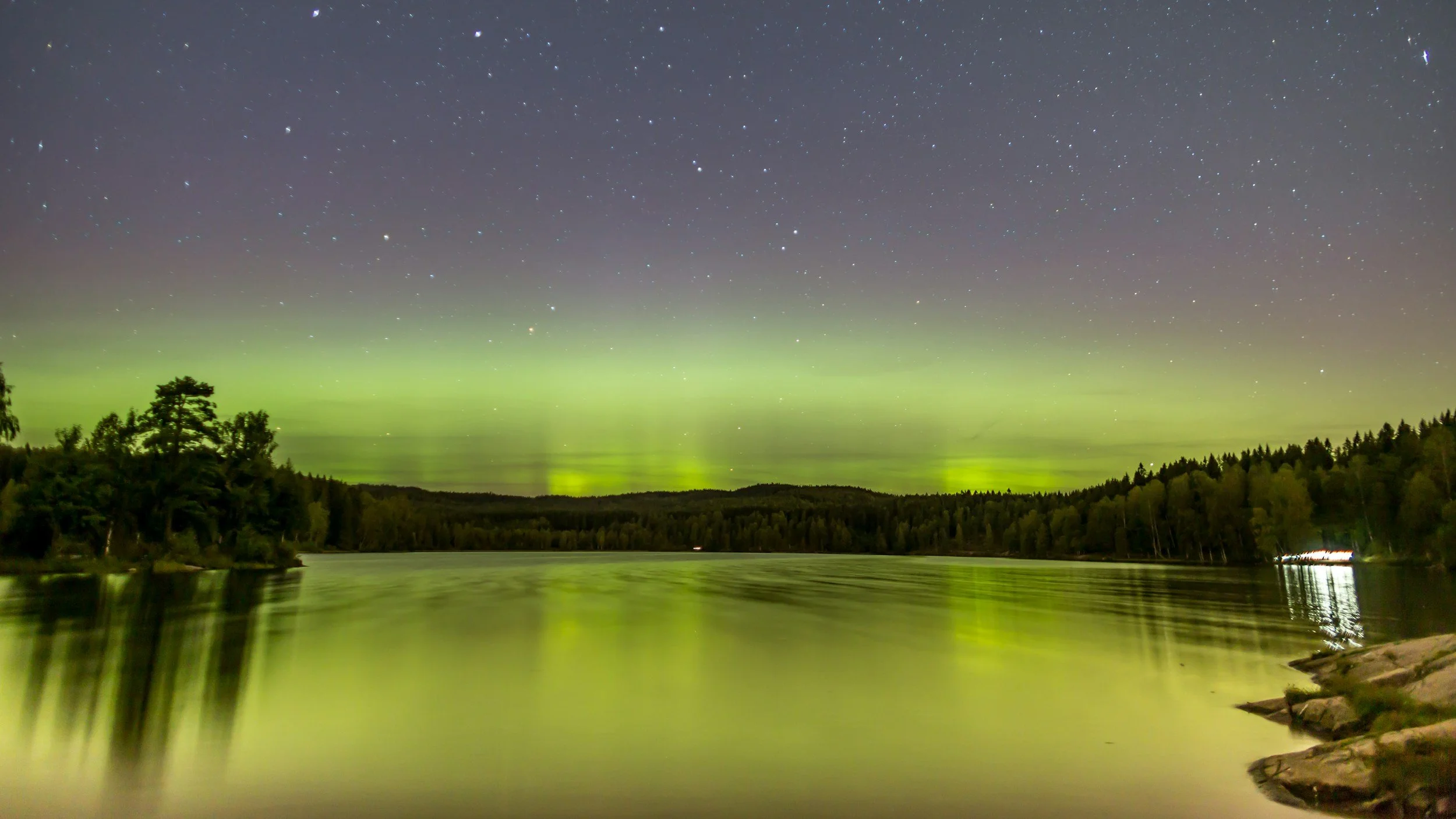 Green northern lights lighting up the stars and skies over the lake at Sognsvann in Oslo during a winternight.