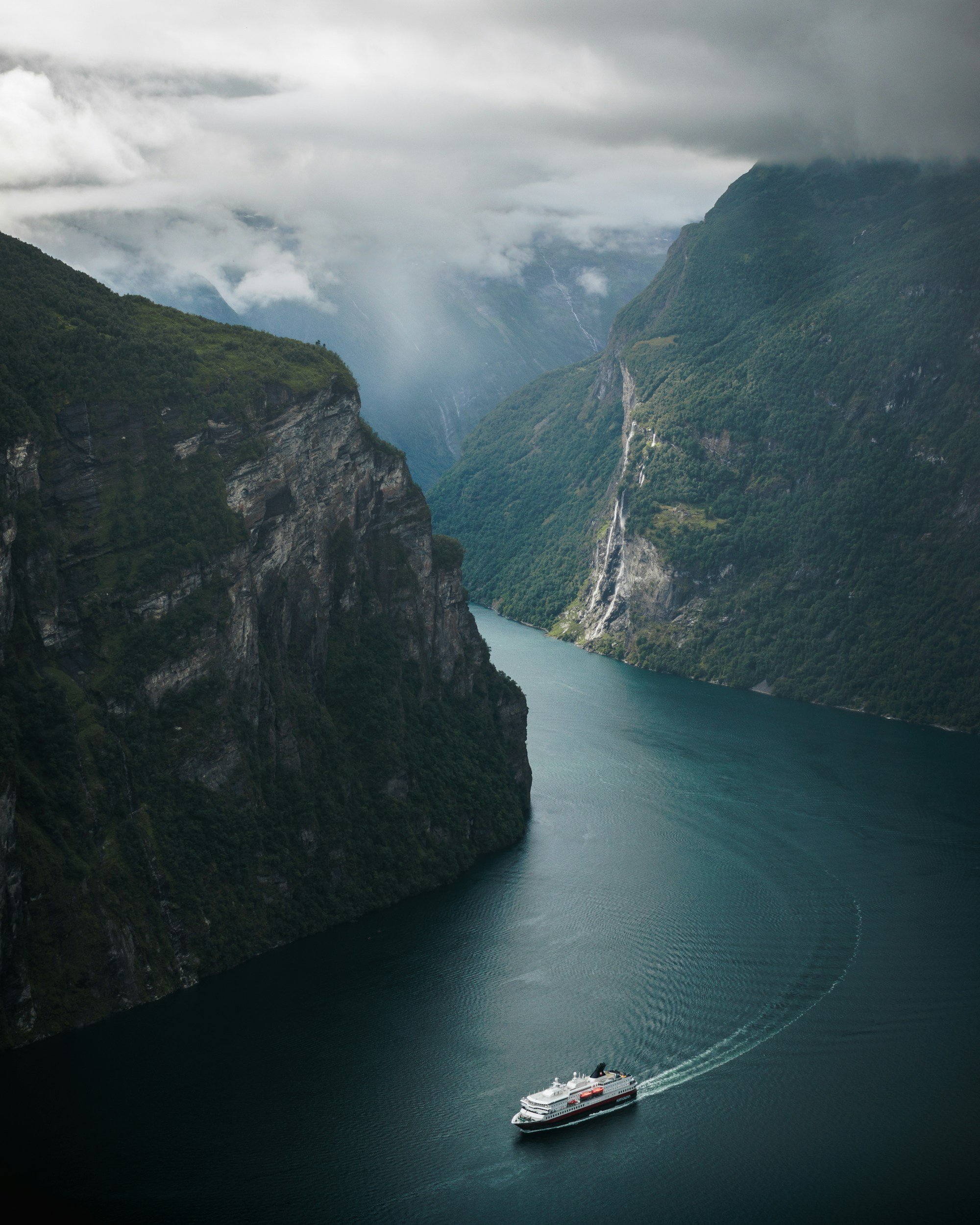 A Hurtigruten ship sailing through the deep fjords in Geiranger.