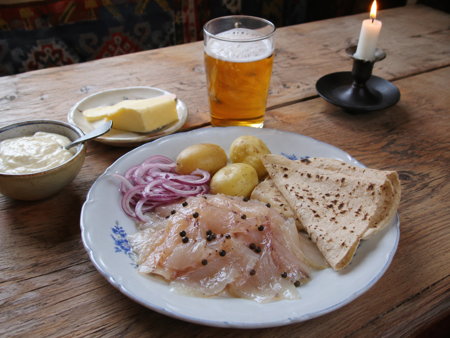 Traditional Valdres rakfisk served with boiled potatoes, lefse, sour cream, red onion and butter on a rustic wooden table.