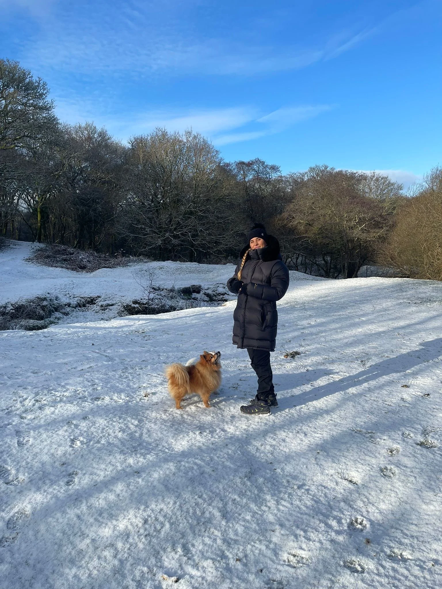 A woman in the snow with two dowgs wearing a thick winter parka, snow boots, insulated pants, wool hat and gloves.
