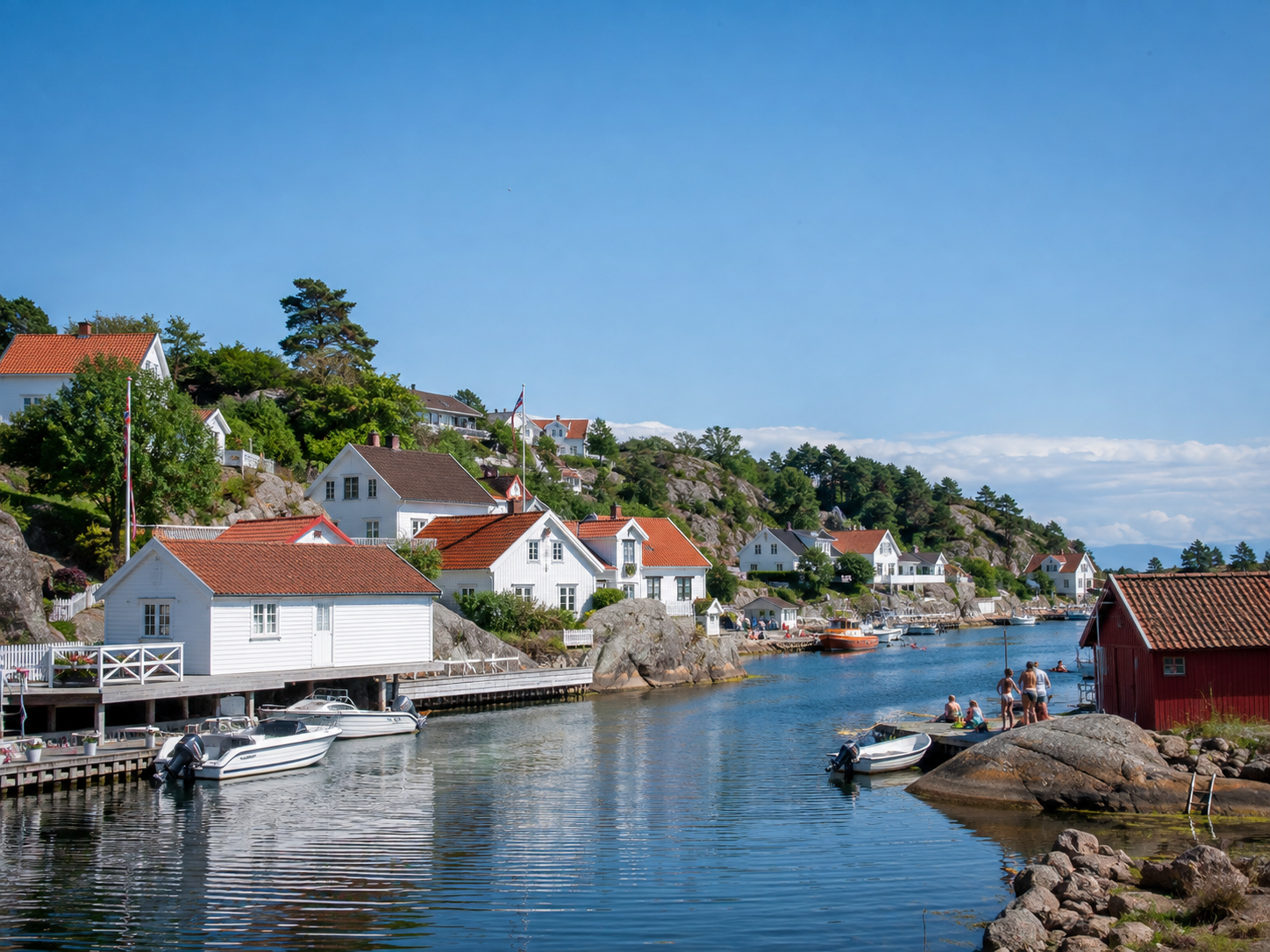 A picture of a little village in southern norway during summer. All the houses are white, people are bathing and there are lots of boats on the water.
