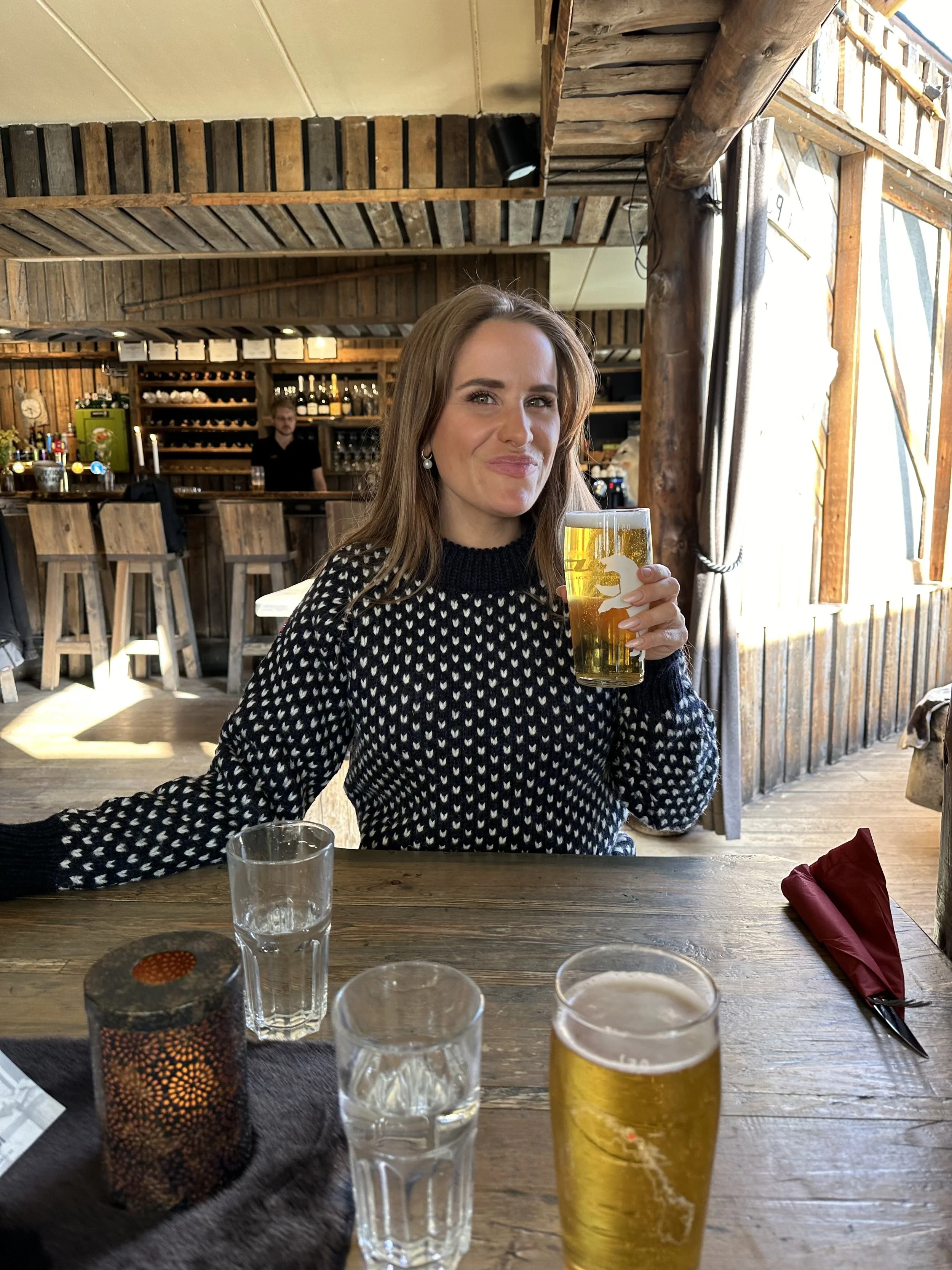 Peron sitting inside a rustic bar in Svalbard, enjoying a glass of Isbjørn beer at a wooden table.