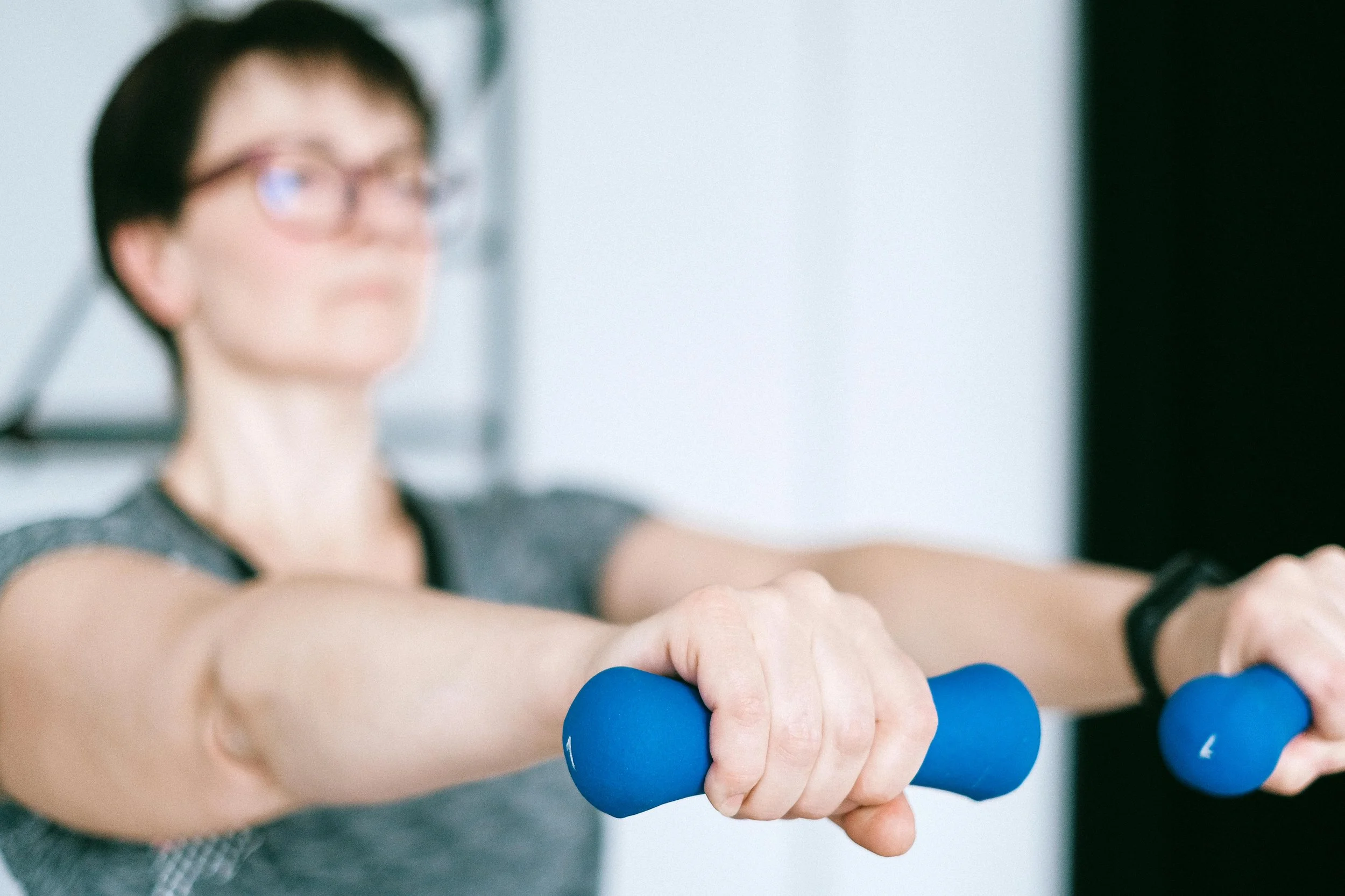 A woman lifts blue hand weights during her physical therapy session