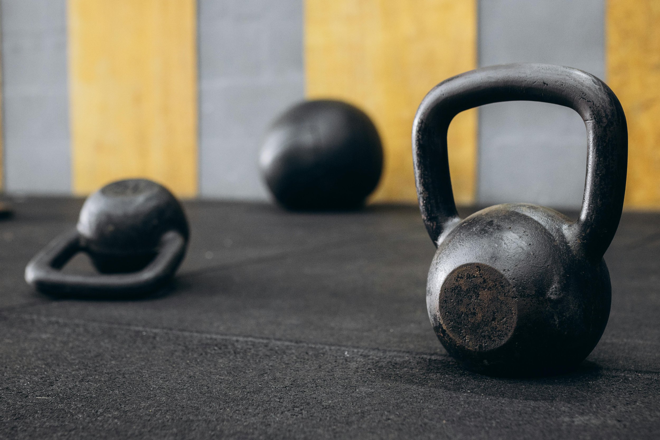 Three iron kettlebells sit in a physical therapy gym