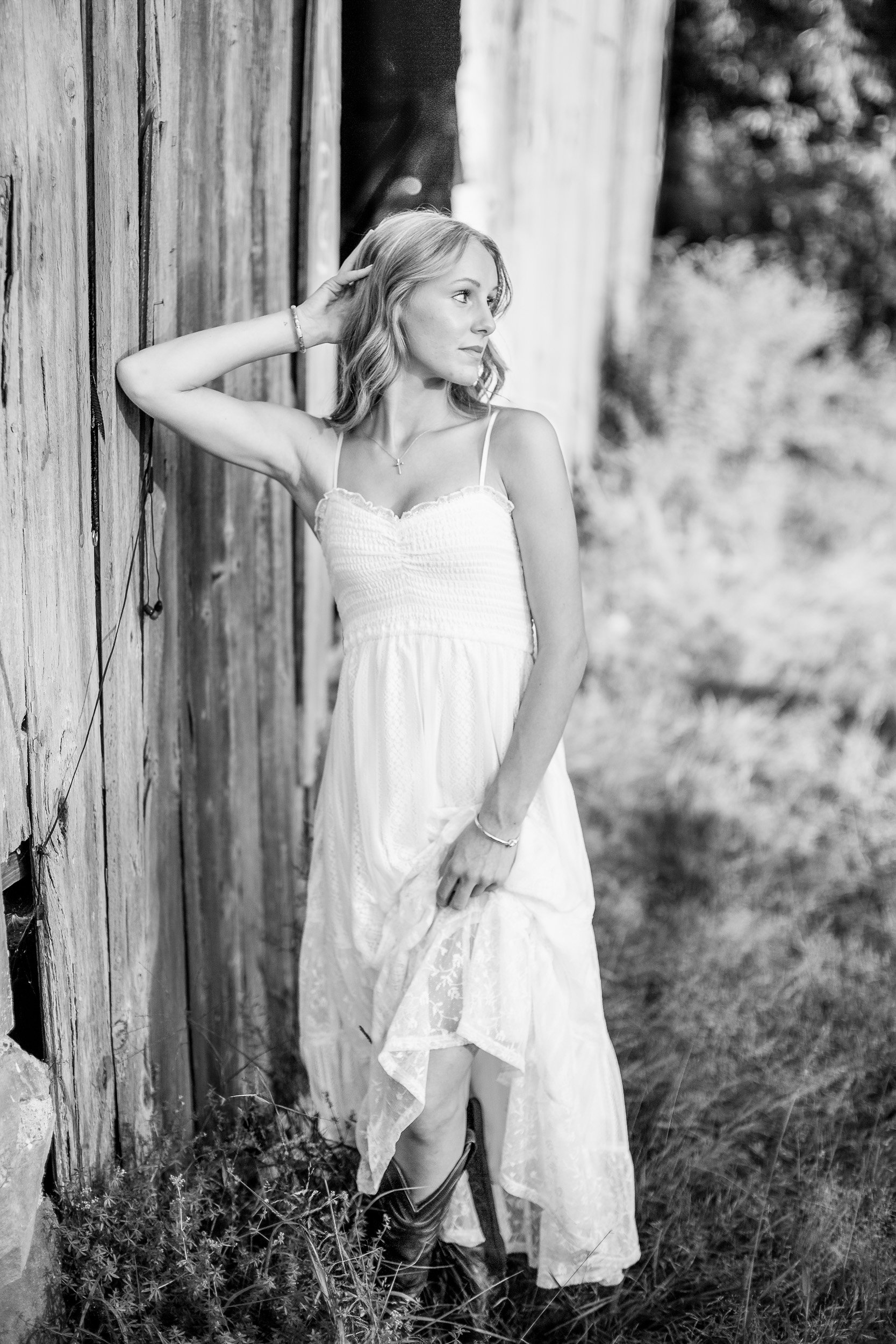 Black-and-white senior portrait of Audrey posing beside a rustic weathered barn.