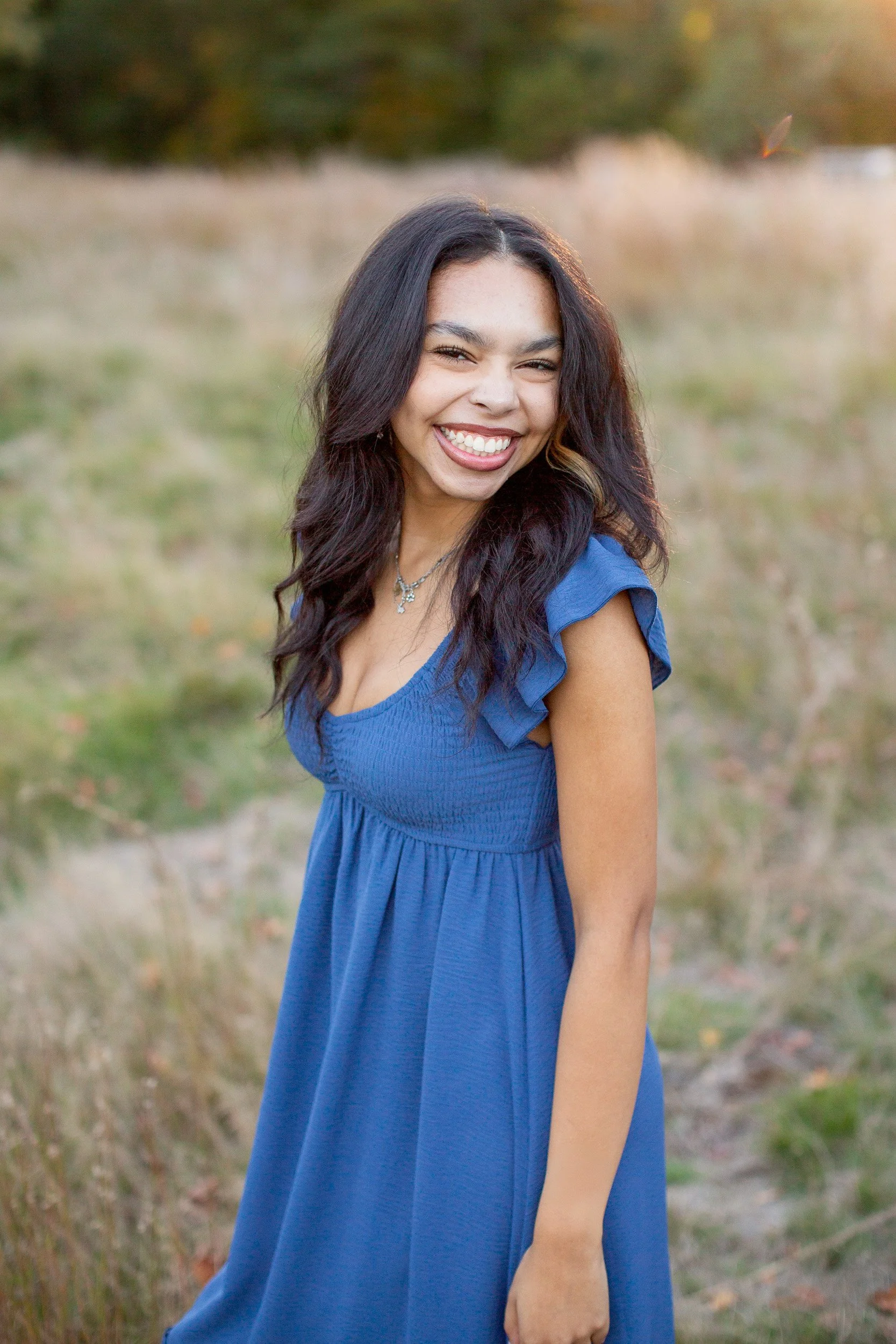 Close-up senior portrait of Maya smiling naturally outdoors.