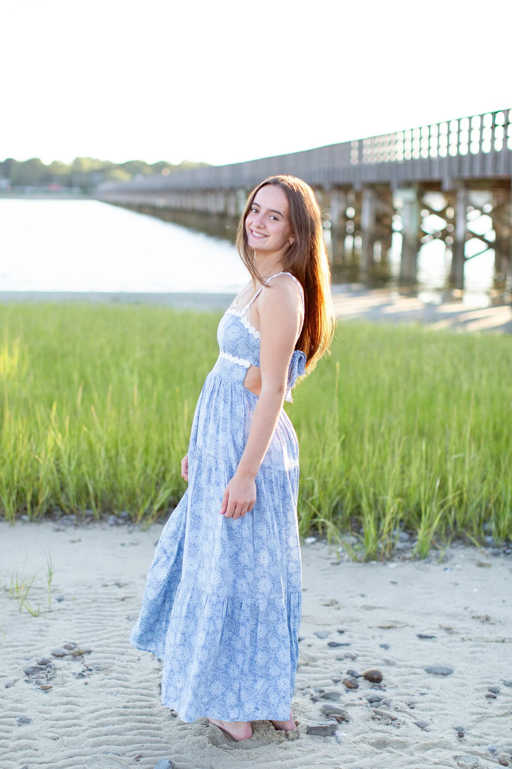 Senior girl in a long blue dress near the wooden bridge at Duxbury Beach