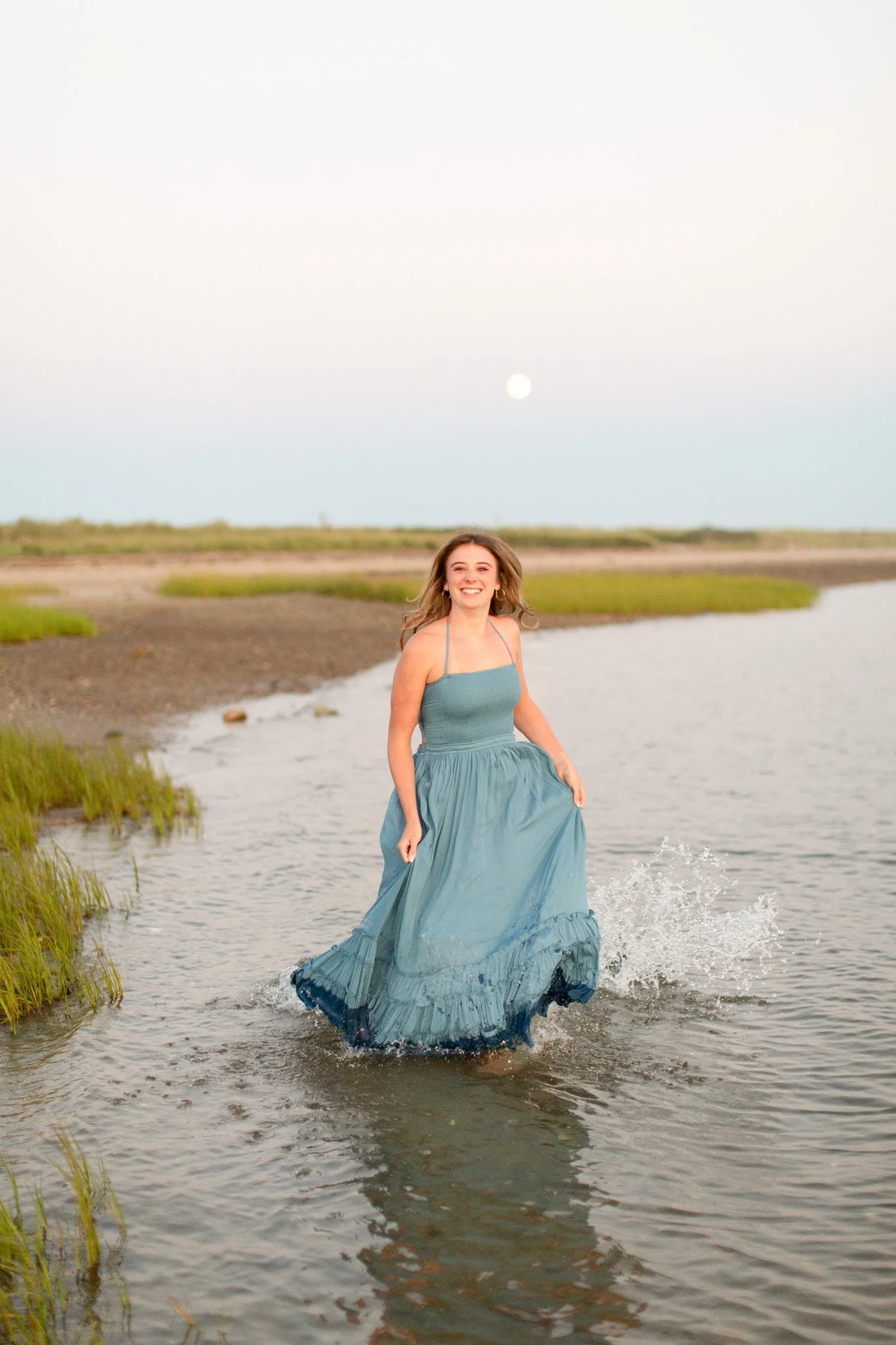 Senior portrait at Duxbury Beach with waves splashing in the water during a summer coastal senior session.