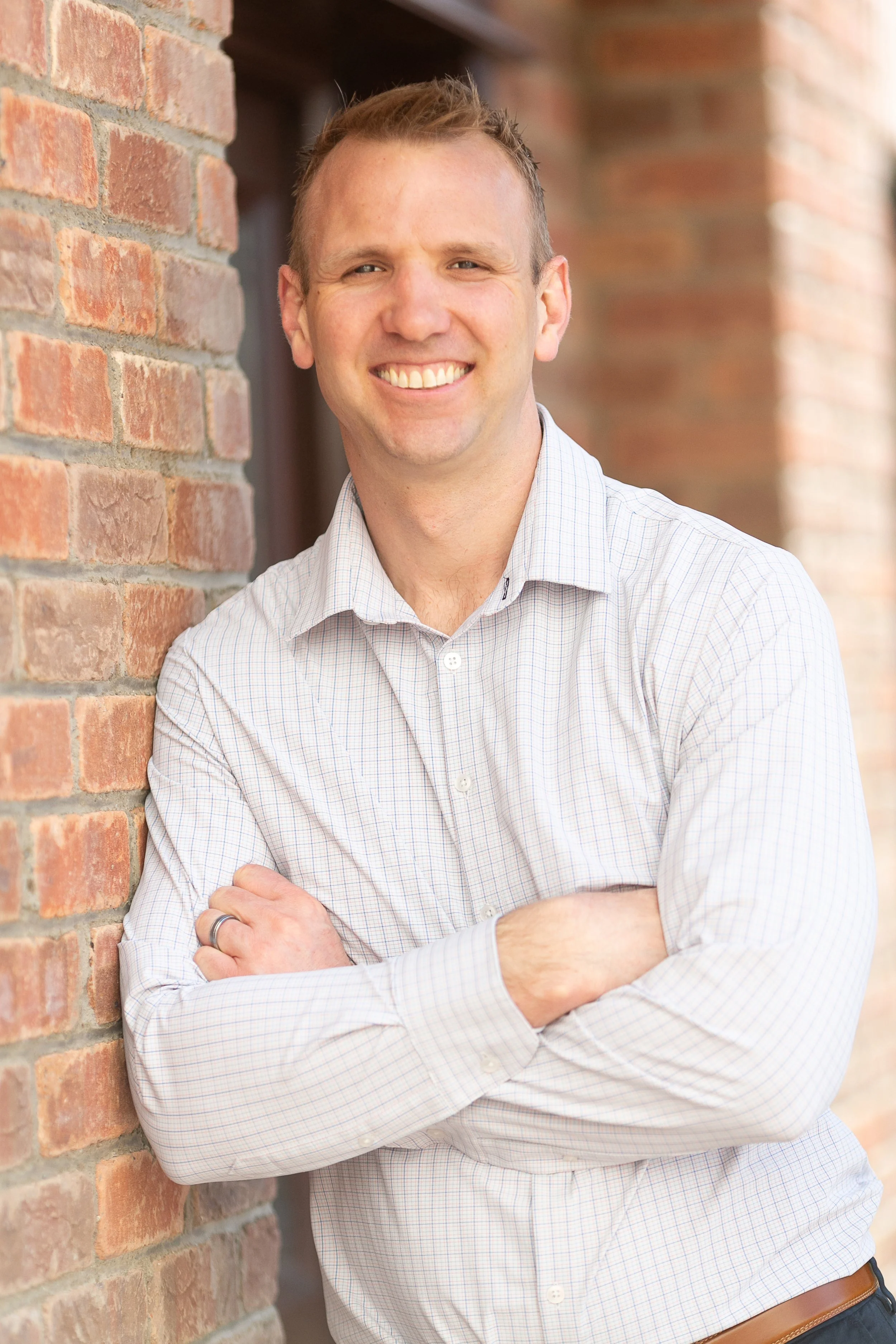 A smiling man with arms crossed leaning against a brick wall.