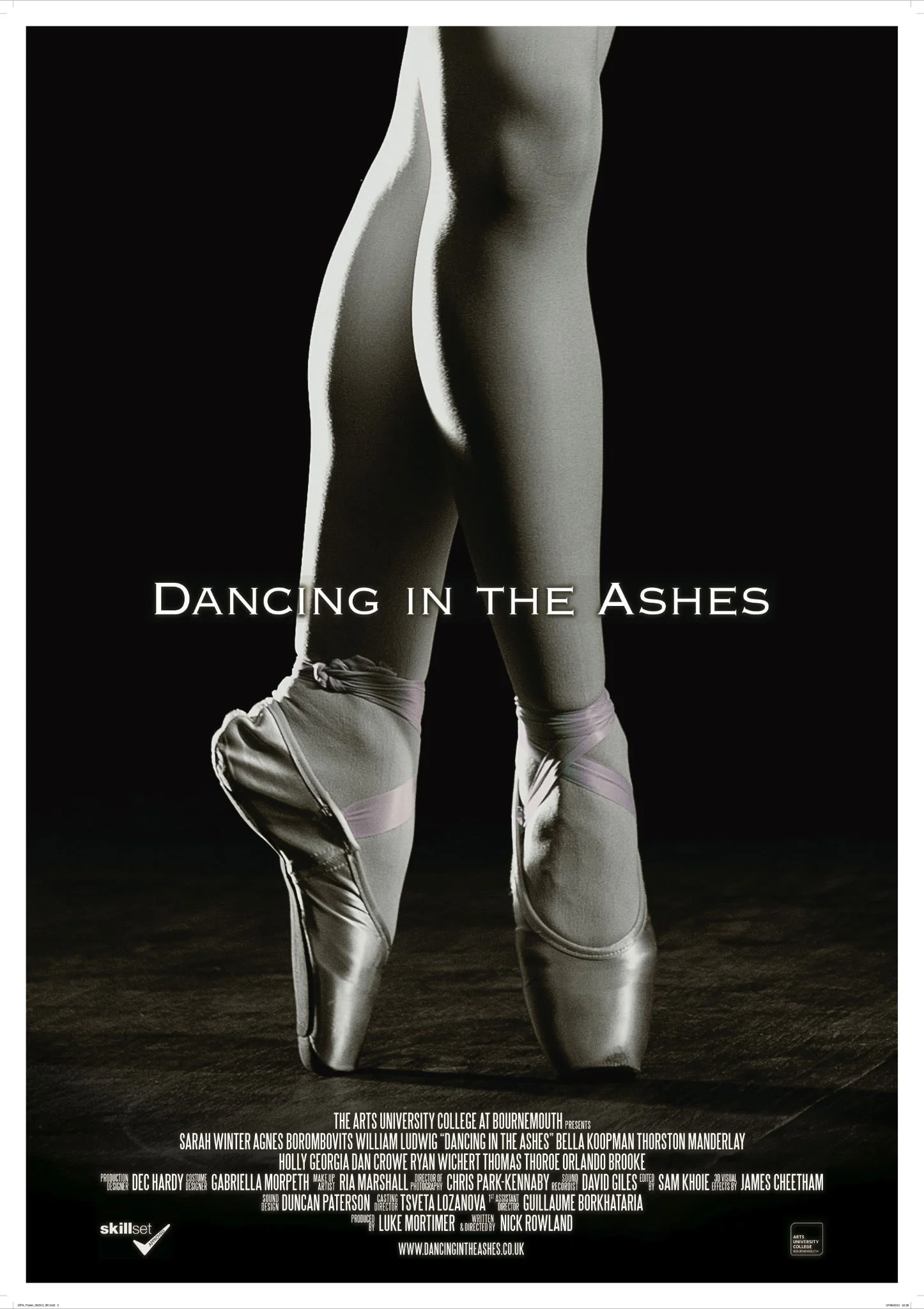 A ballet dancer's legs and feet en pointe in satin shoes with ribbons, with the shadowed background highlighting the musculature and pose, promoting the production 'Dancing in the Ashes'.