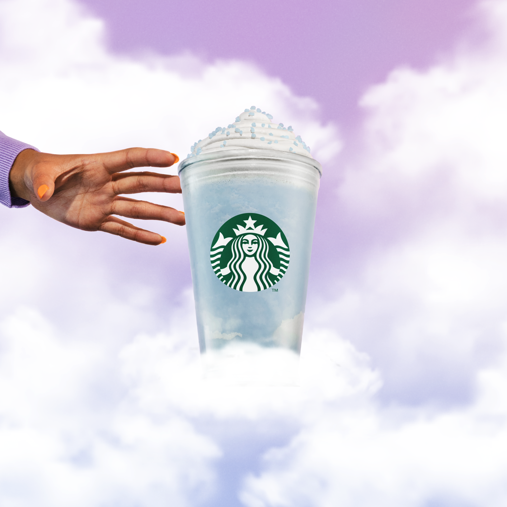 Hand with orange nail polish reaching towards a Starbucks unicorn frappuccino in the sky with clouds.