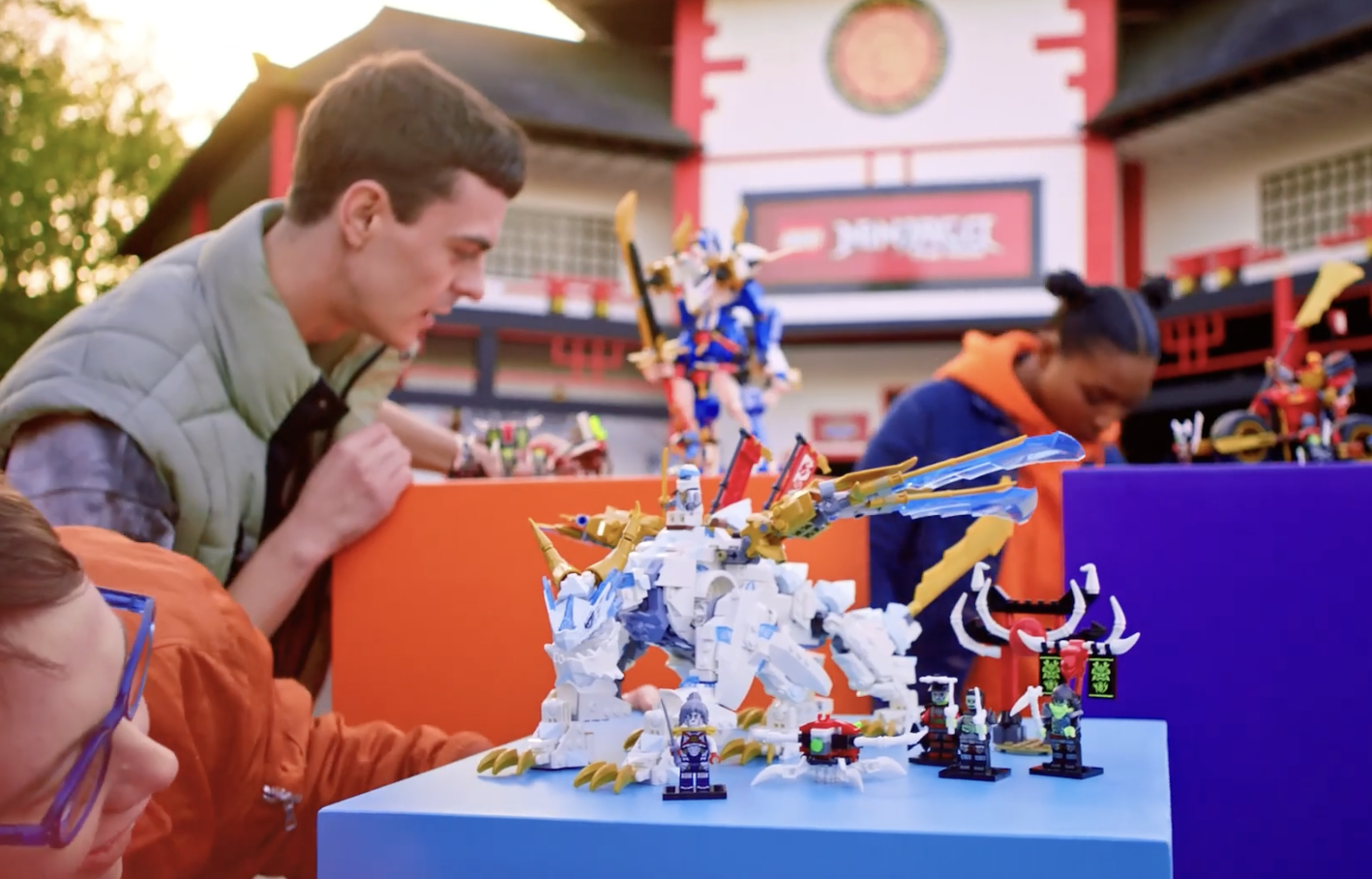 People looking at and admiring Lego models of mythical and fantasy creatures on display at an outdoor event, with a colorful building in the background.