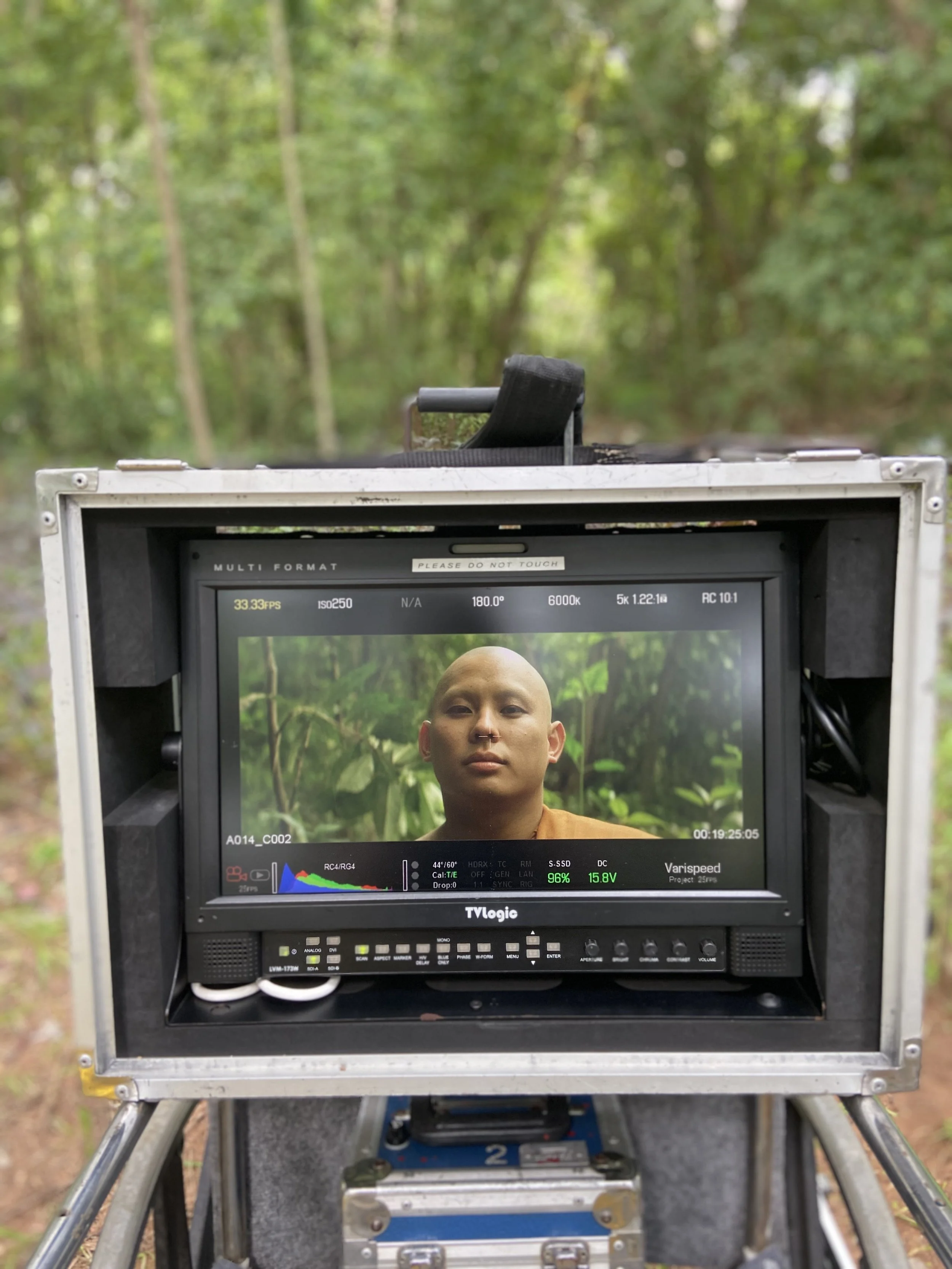 A person being filmed or photographed in a forest, seen on a monitor screen on set.