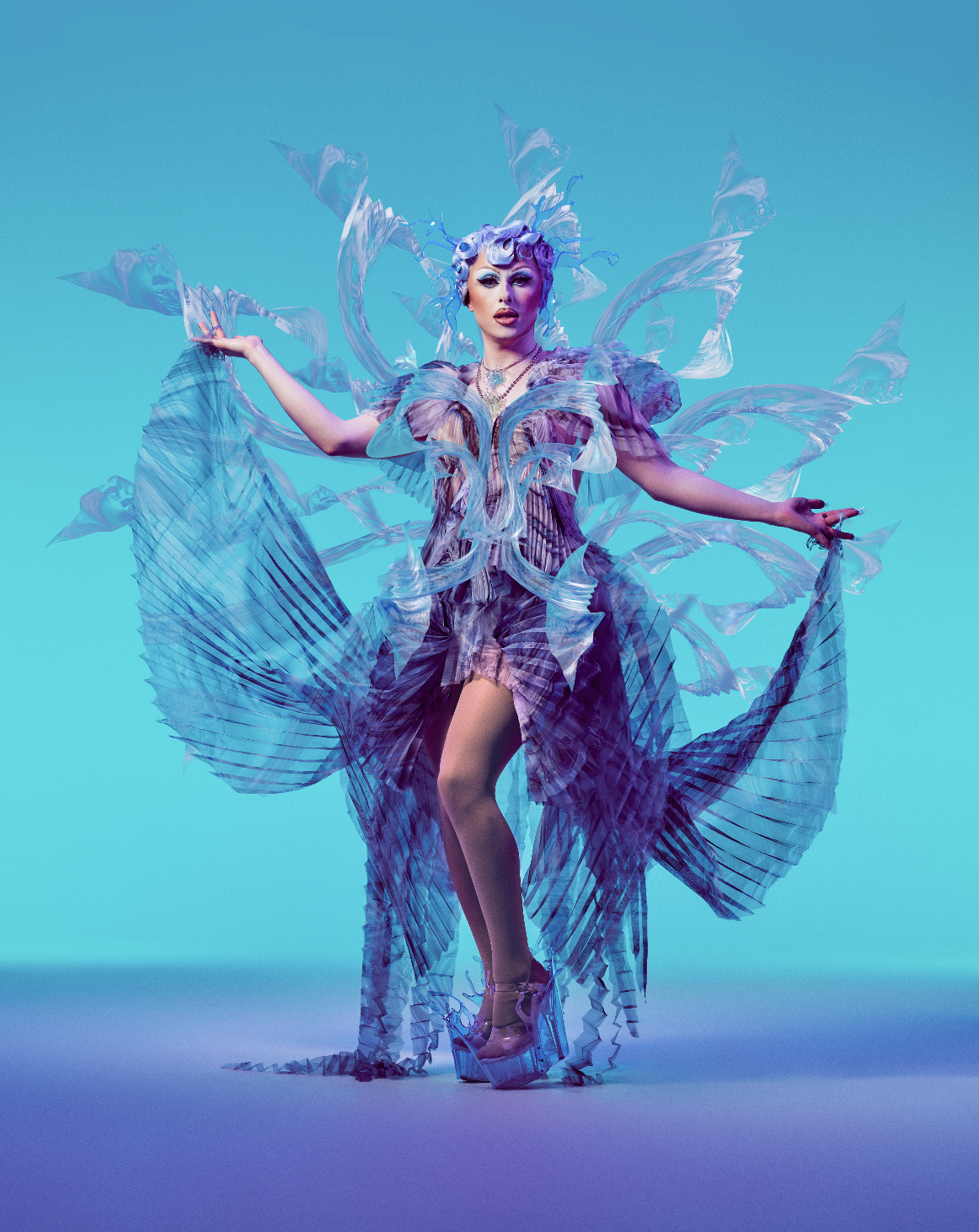 A person dressed in elaborate, futuristic costume with flowing, iridescent fabric and large, wing-like extensions, posing against a gradient blue background.