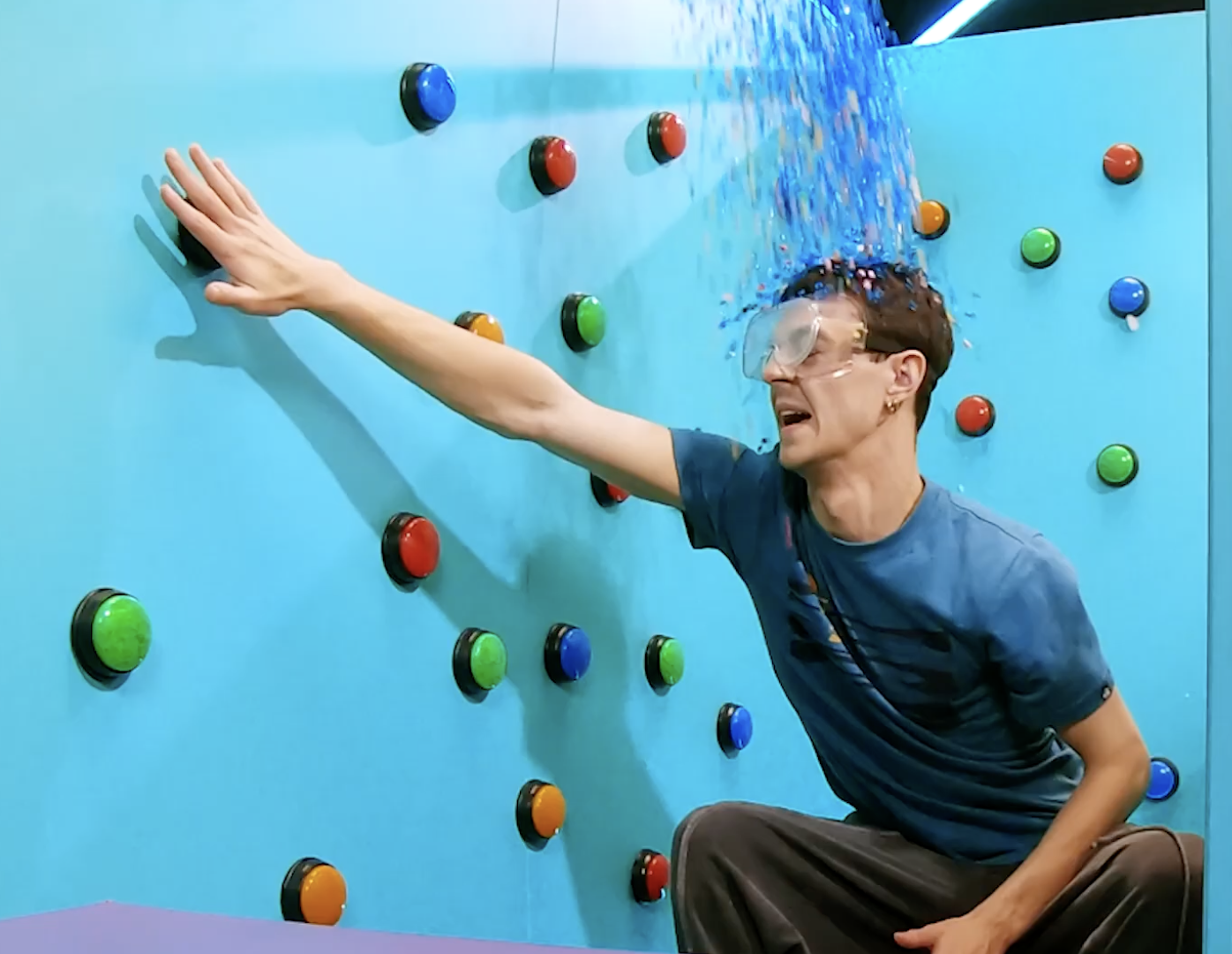 Person in goggles falling against a wall with colorful buttons during a splash wall activity.