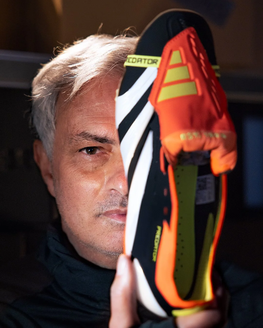 Jose Mourinho with short gray hair holding a colorful running shoe in front of his face.