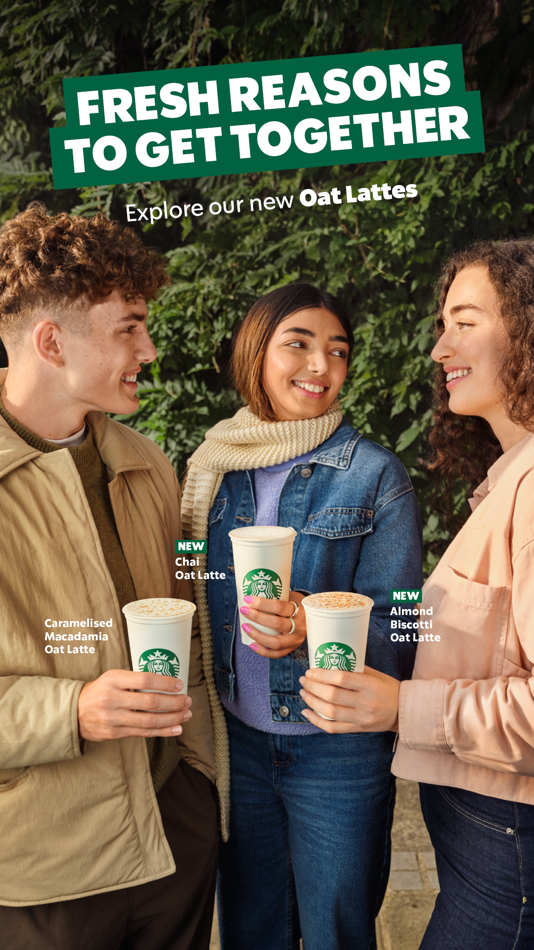 Three people holding Starbucks oat lattes, smiling, with a green leafy background. There are labels indicating new oat latte flavors, including caramelized macadamia, chai, and almond biscotti.