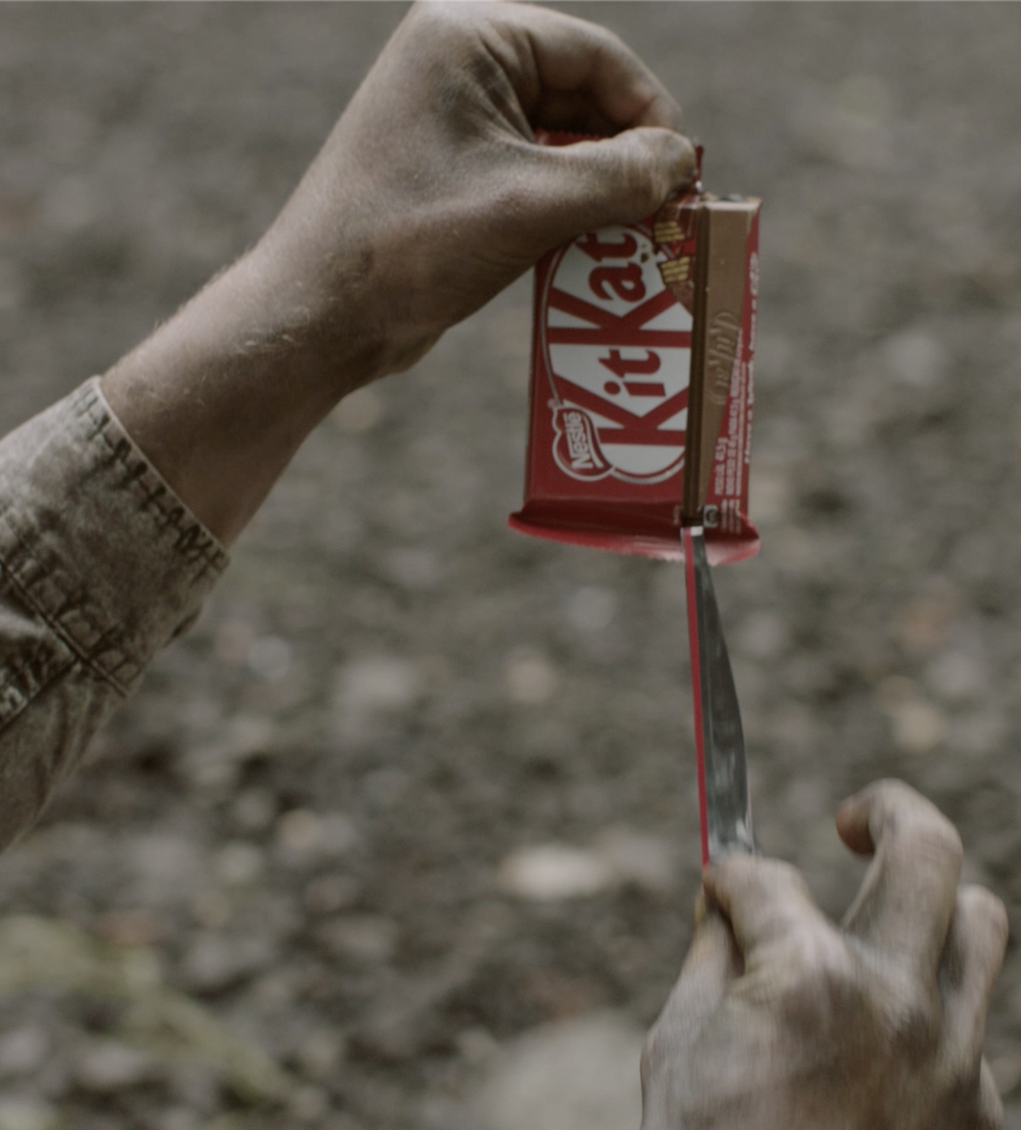 A person using a knife to cut open a Kit Kat candy bar outdoors.