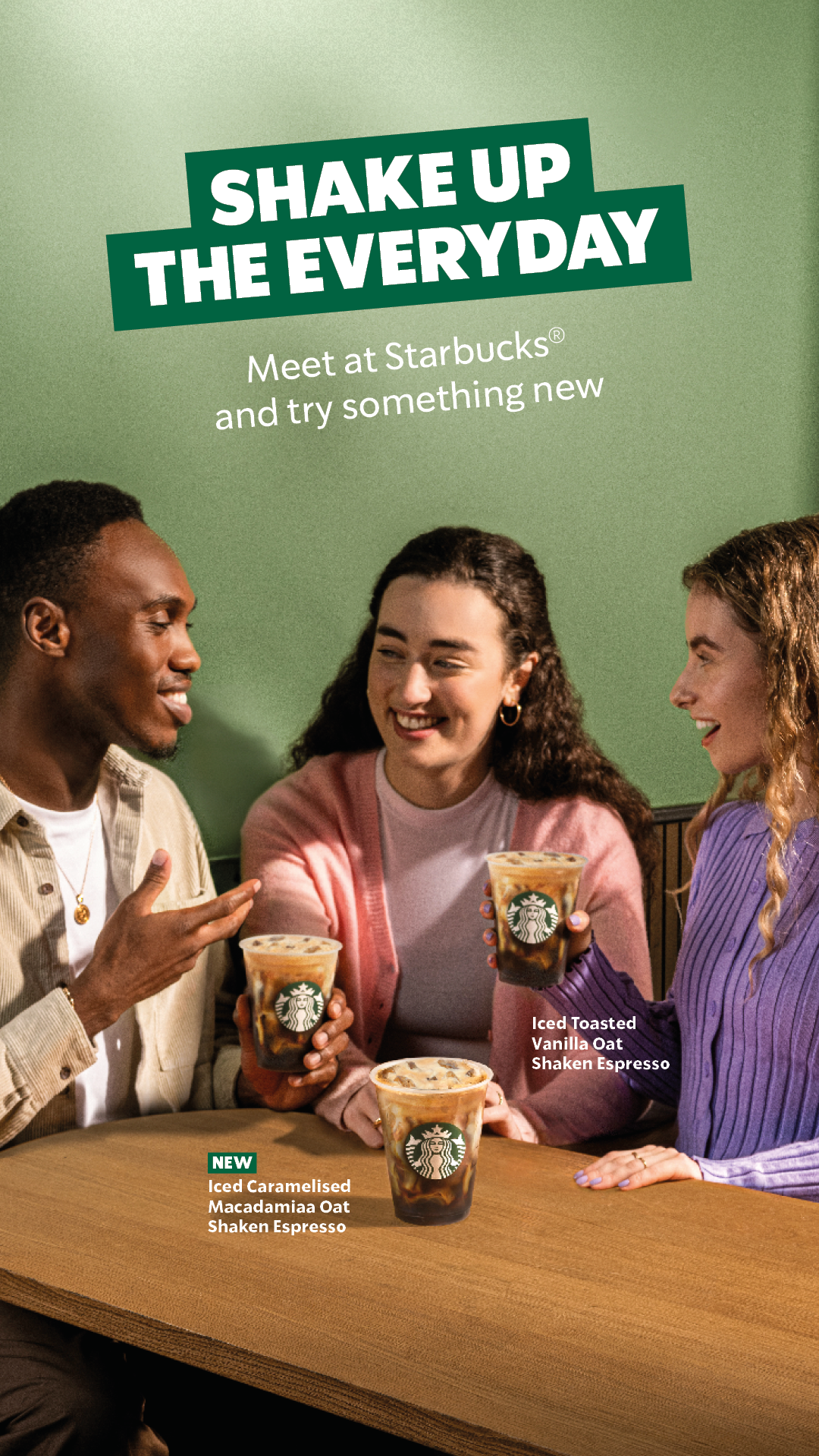 Three people sitting at a table in a Starbucks, holding iced coffee drinks, and smiling at each other, with a green background and promotional text for new drink flavors.