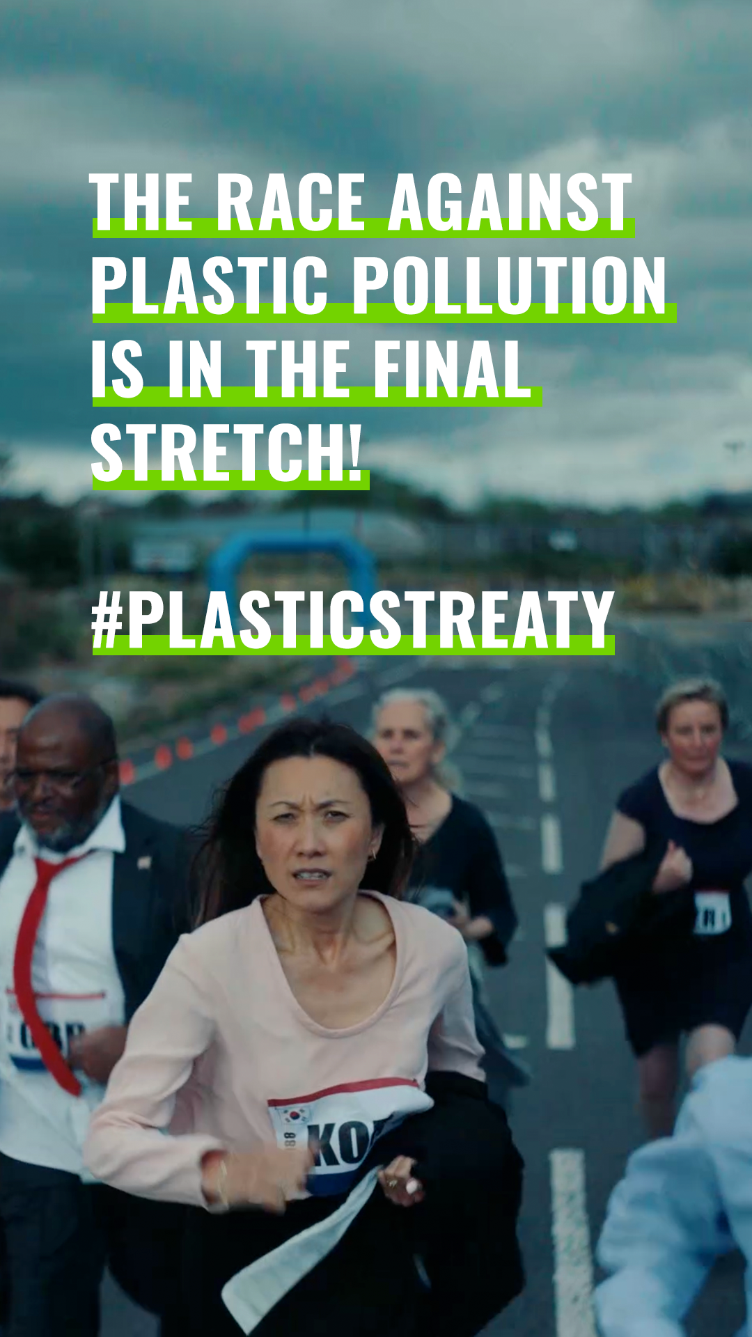 Group of runners participating in a race on a road with an overcast sky, making an effort to finish in a Greenpeace social campaign.