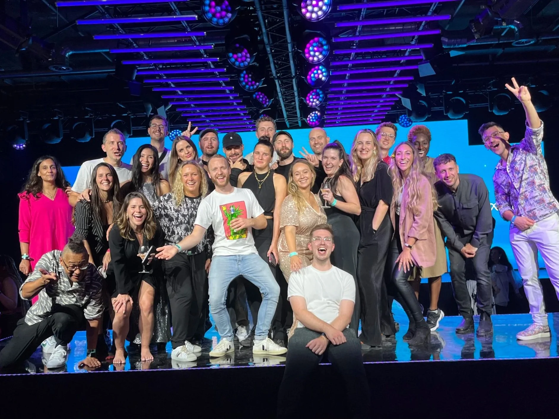 Group of people celebrating on stage at an event, smiling and posing for a photo with stage lighting and a blue background.