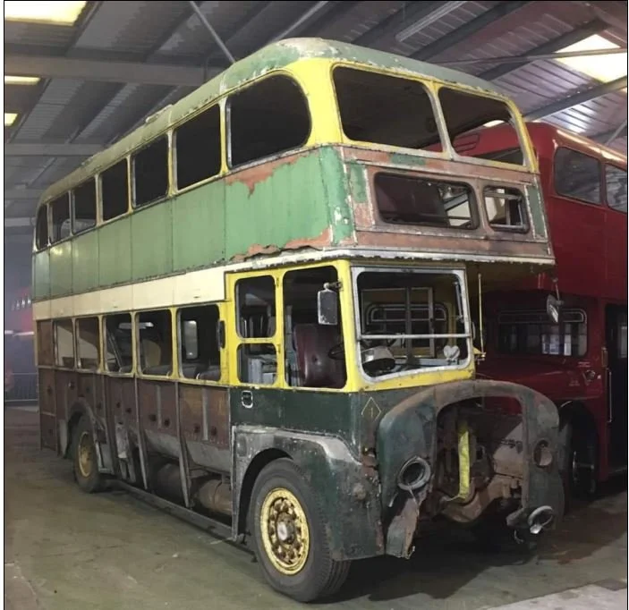 An old, rusty double-decker bus with faded green and yellow paint inside a warehouse.