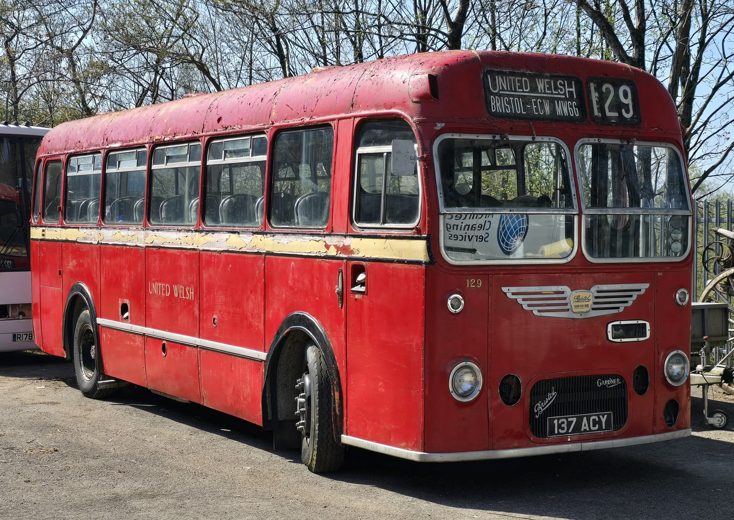 An old red bus with the number 129, labeled 'United Welsh', parked outdoors with trees in the background.