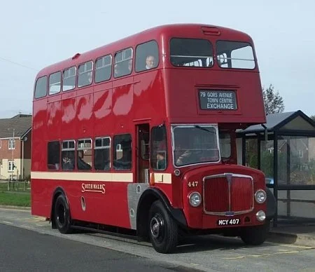 A red double-decker bus parked at a bus stop with a sign indicating it is en route to Tower Hill Exchange.