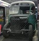 Old green truck with a chain-link fence in front, parked outdoors.