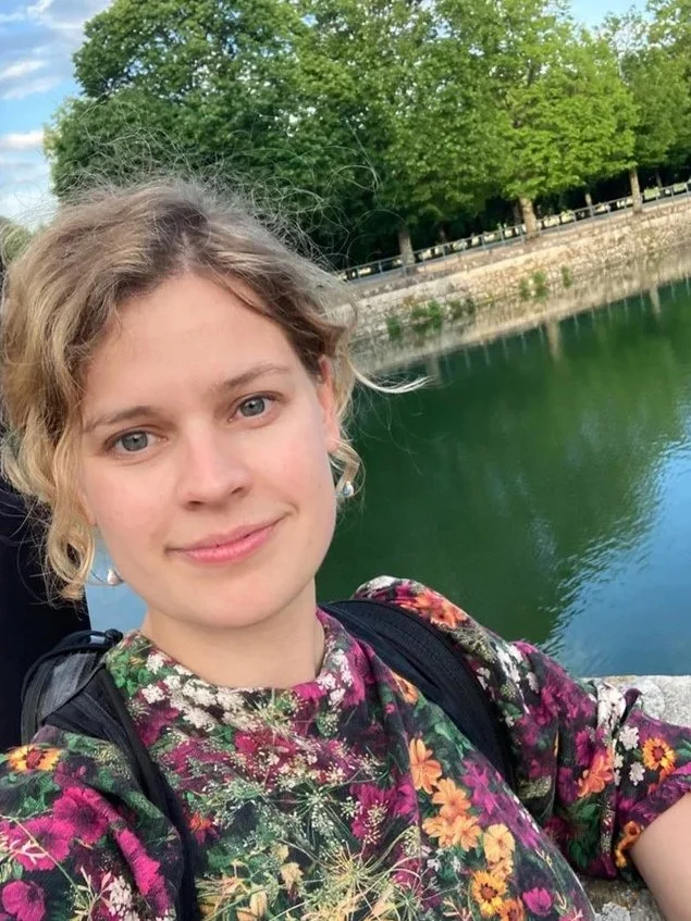 Portrait of violinist Léna Ruisz smiling outdoors by a river, informal headshot for her online violin teaching studio.