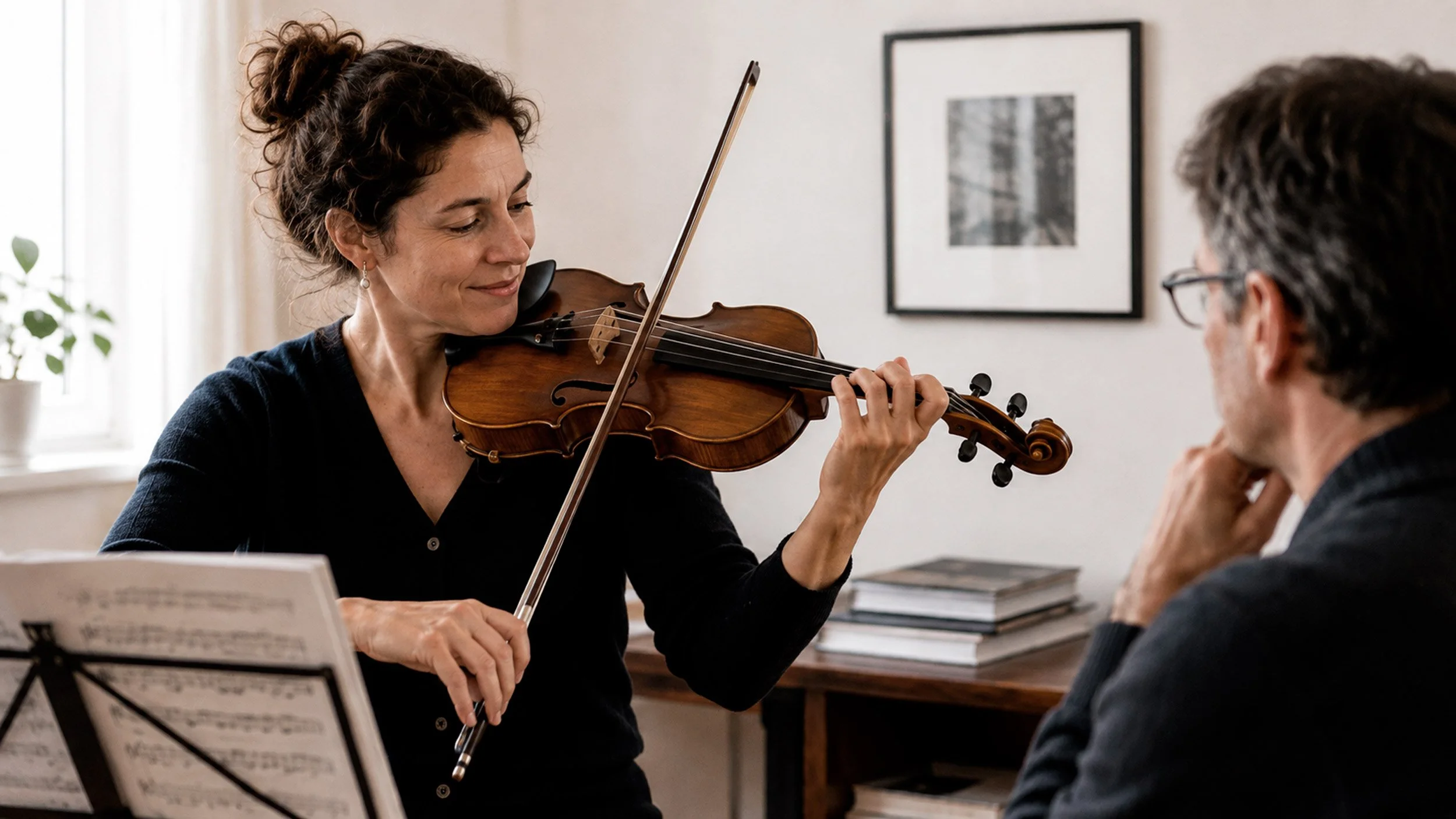 A violinist plays in a bright room while a seated listener watches, the condition at the heart of violin performance anxiety.