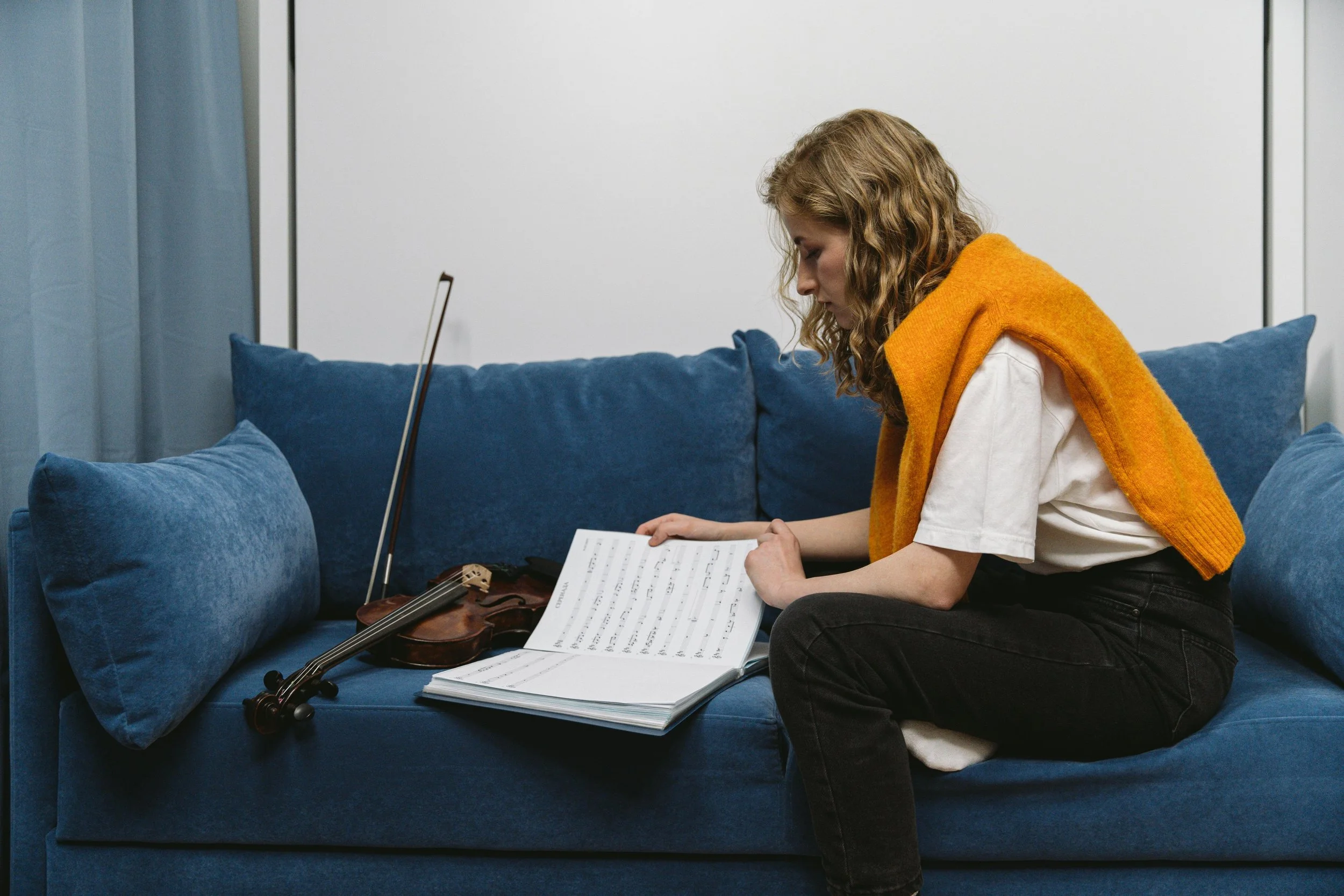 Adult violinist reading a score on the sofa with their instrument beside them.
