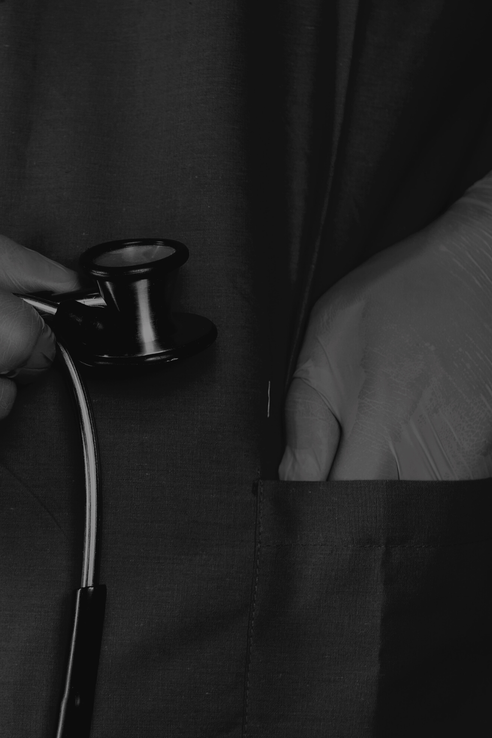 Close-up of a healthcare worker wearing gloves holding a stethoscope against a dark fabric background.