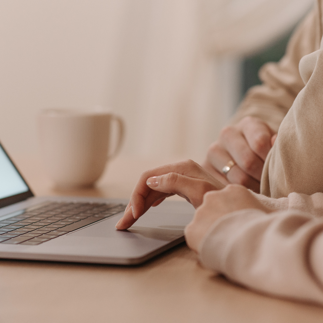 Close-up of a person typing on a laptop keyboard with a beige coffee mug in the background.