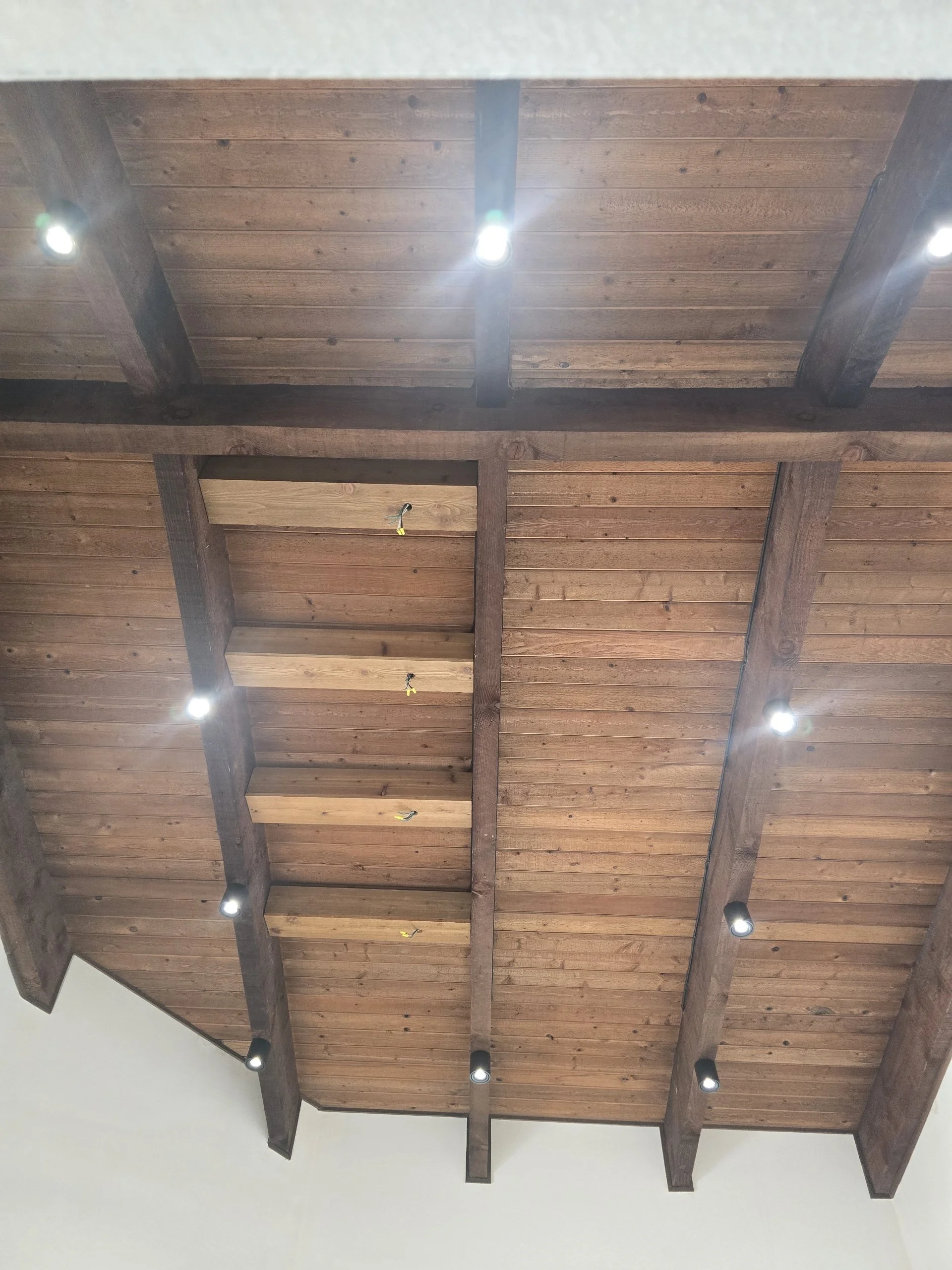 Ceiling with wooden beams and wooden planks, illuminated by multiple small spotlights.