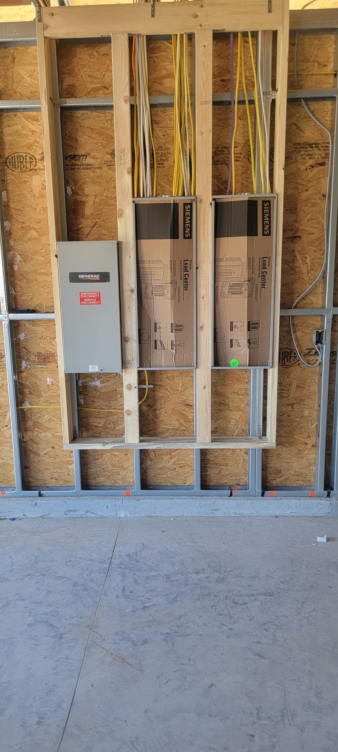 Construction site with electrical wiring, load center boxes, and electrical panel mounted on a wooden wall frame.