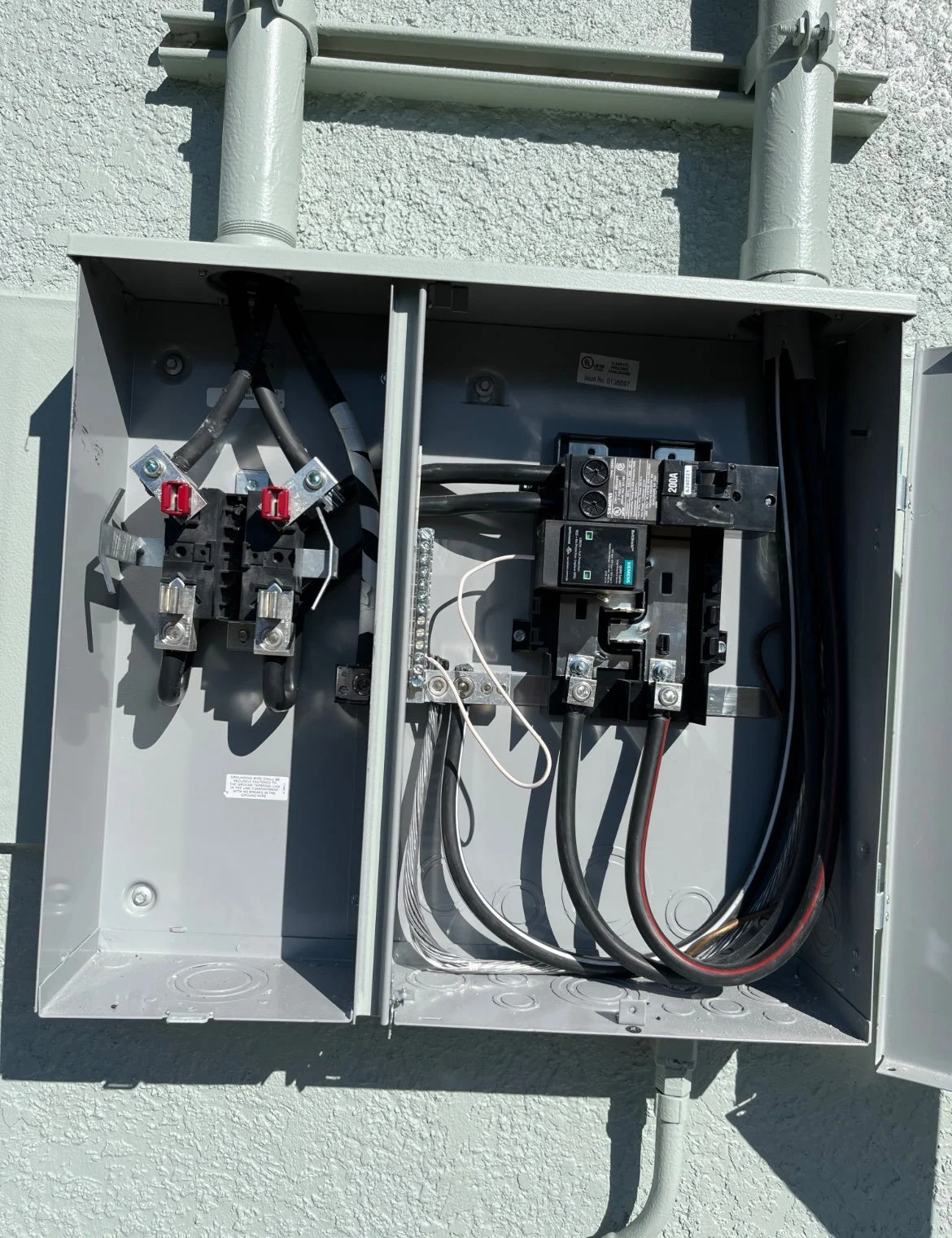 Open electrical utility box containing circuit breakers, wires, and connectors mounted on an exterior wall.
