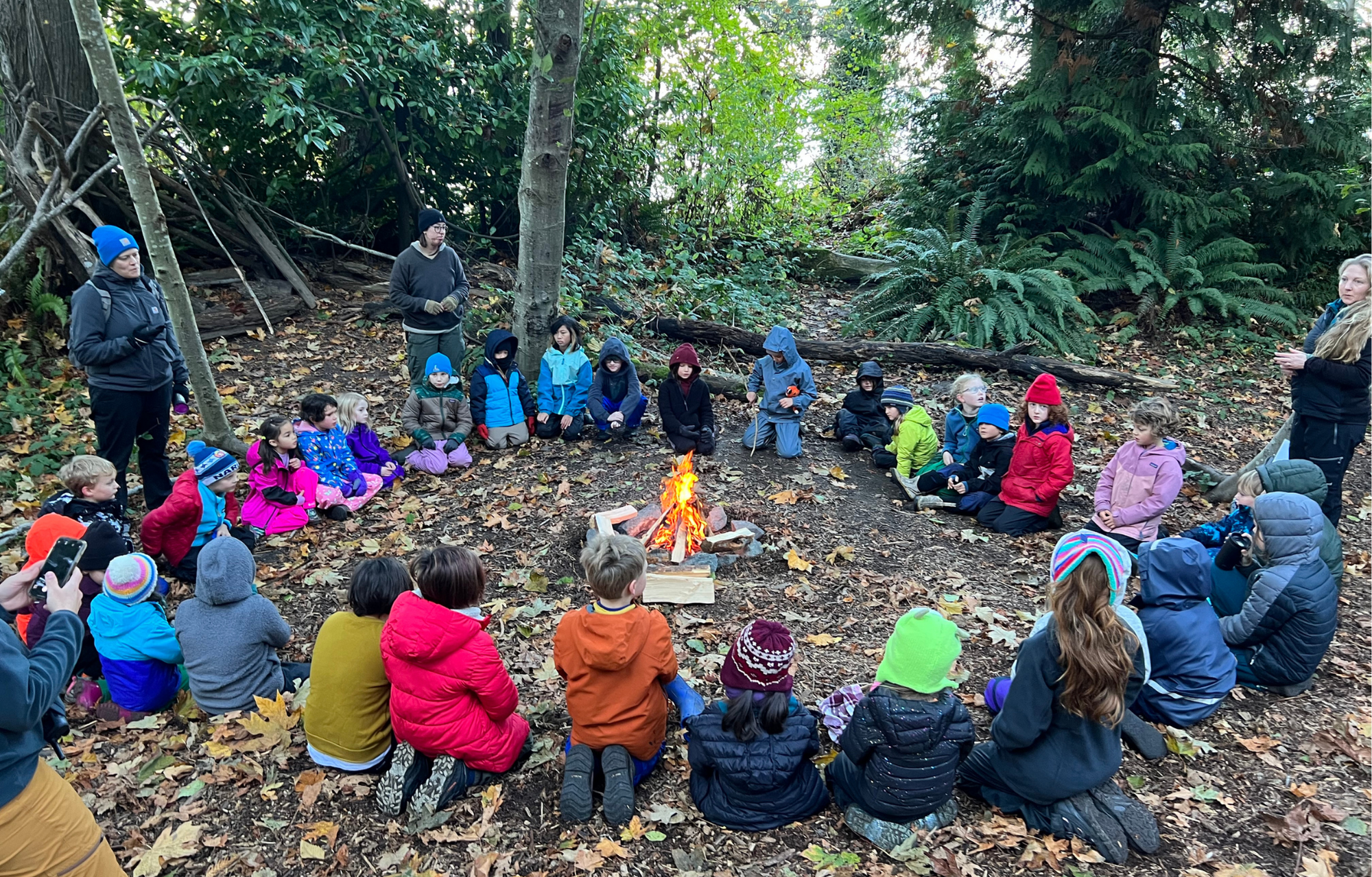 Circle of children and parents around a campfire.
