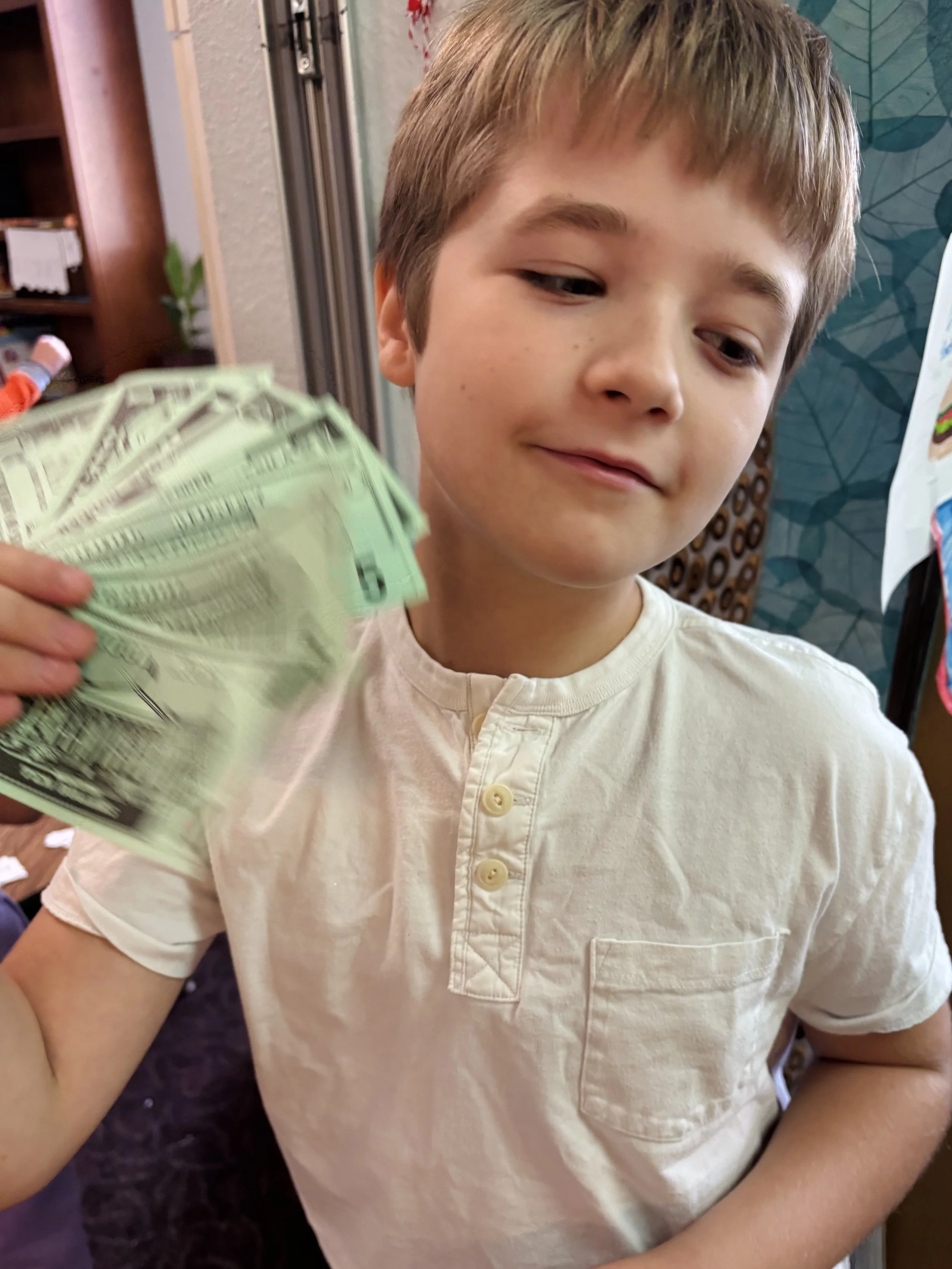 A young boy holding a fan of cash, looking slightly to the side with a neutral expression.