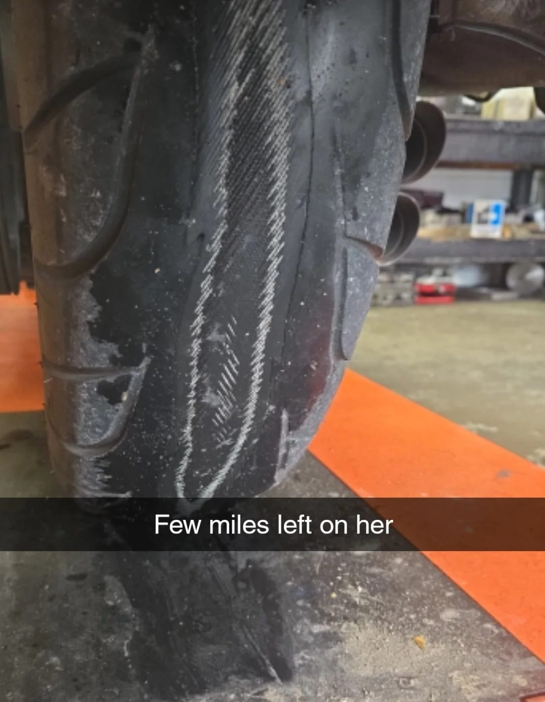 Close-up of a worn motorcycle tire with visible tread marks and signs of use, on a workshop floor.