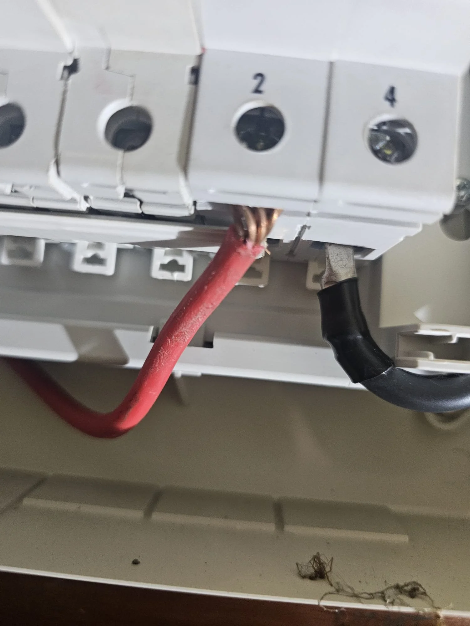 Close-up of bare copper conductor stripped too far and left exposed outside an MCB terminal in an old consumer unit