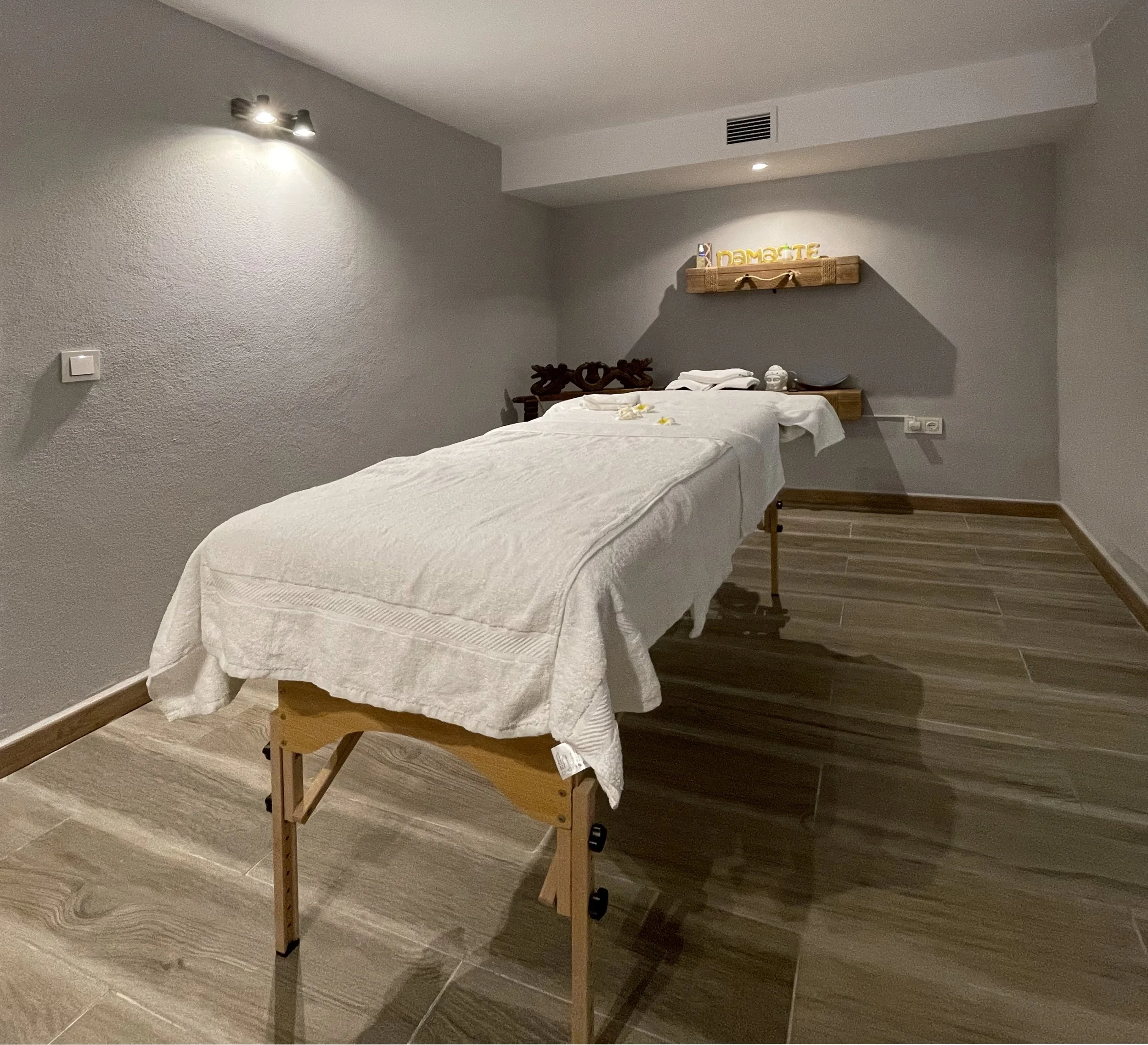 Tafelmassage met een tafel en een houten rek met de letters 'namaste' boven de tafel, decoraties en handdoeken.