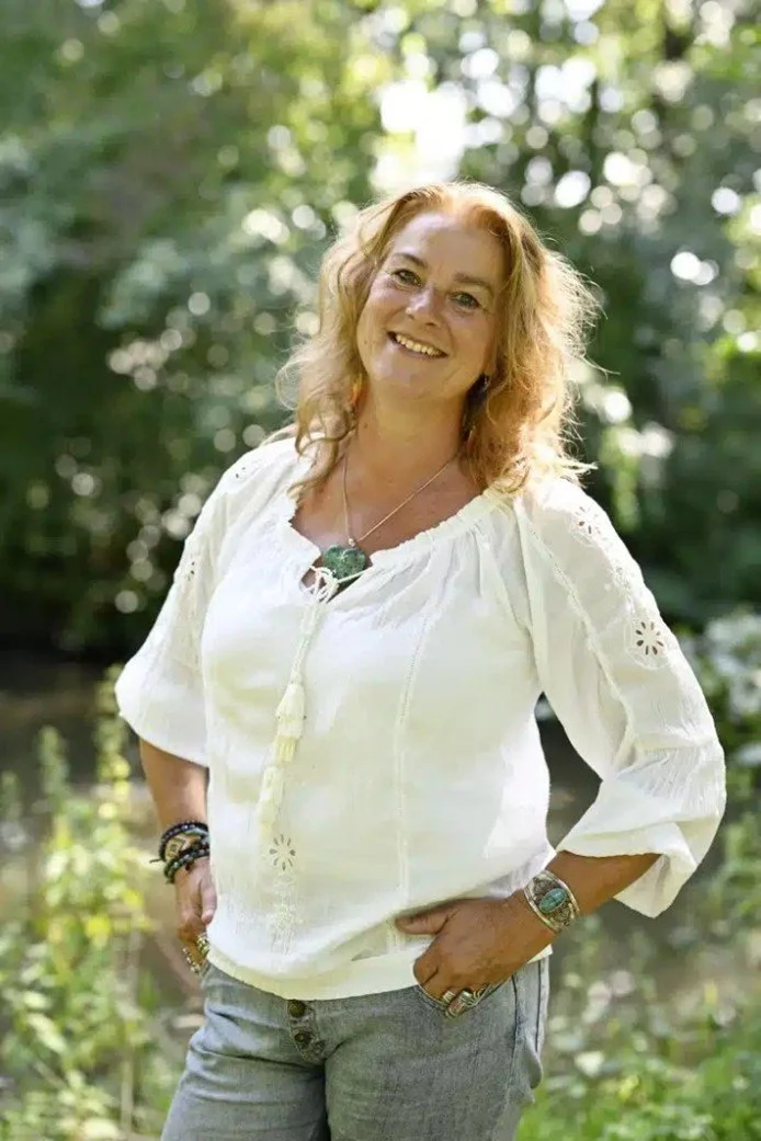 Vrouw met knalroze haar die buiten in de natuur staat en lacht.