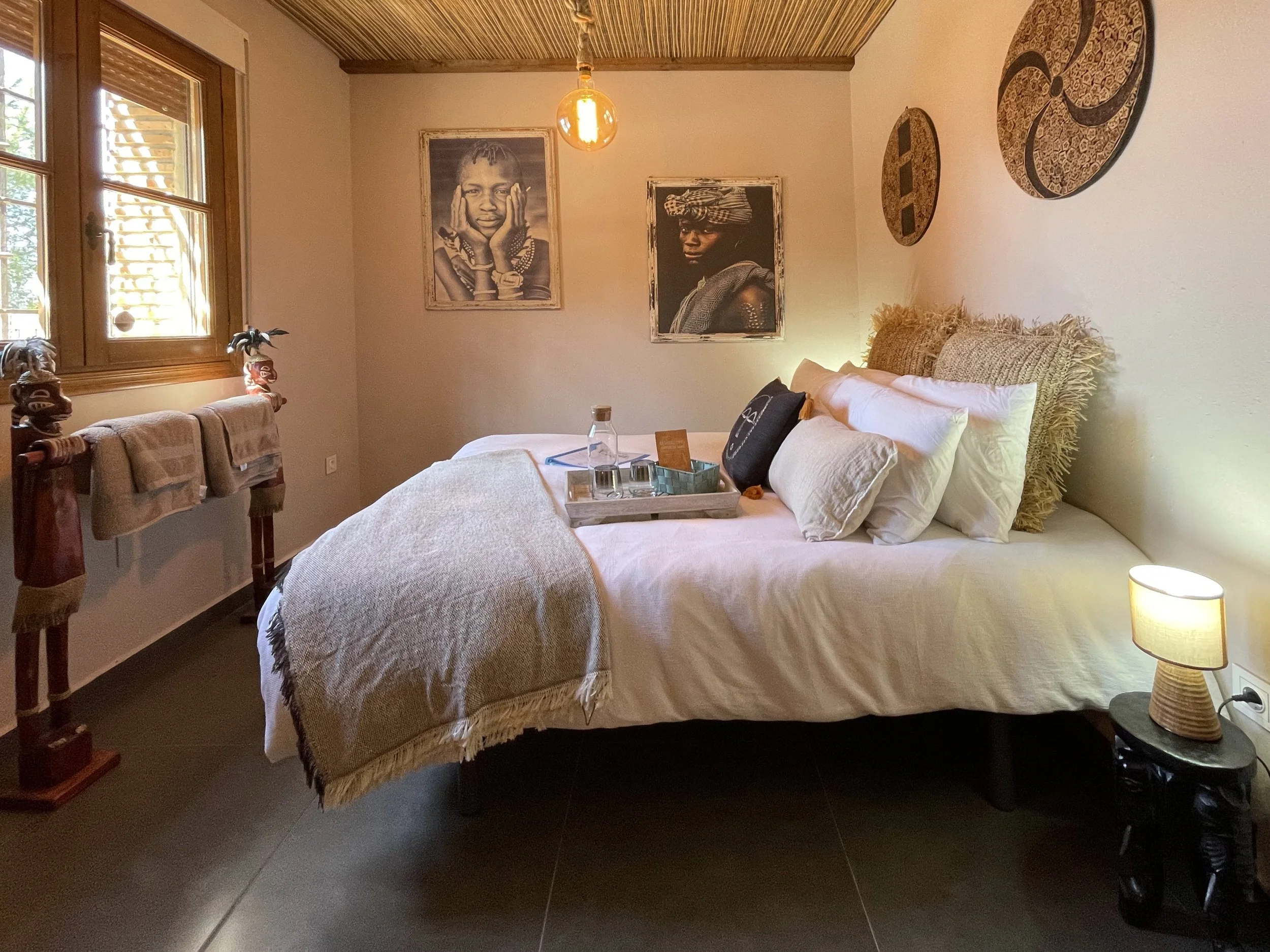 Een slaapkamer met een bed, een nachtkastje, foto's en decoraties aan de muur, en een raam met houten jaloezieën.
