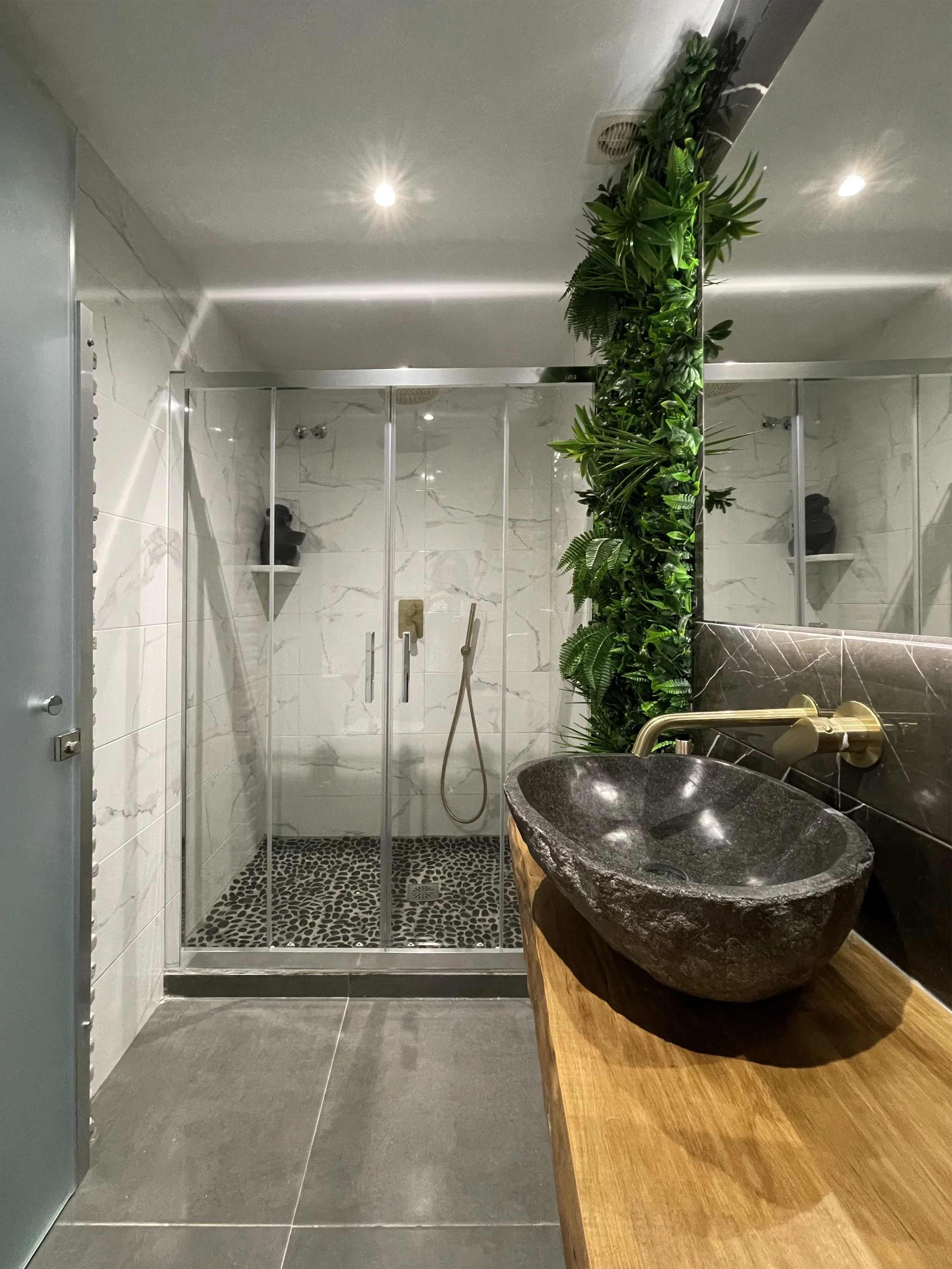 Moderne badkamer met een inloopdouche, een stenen wastafel op een houten blad en groene planten langs de muur.