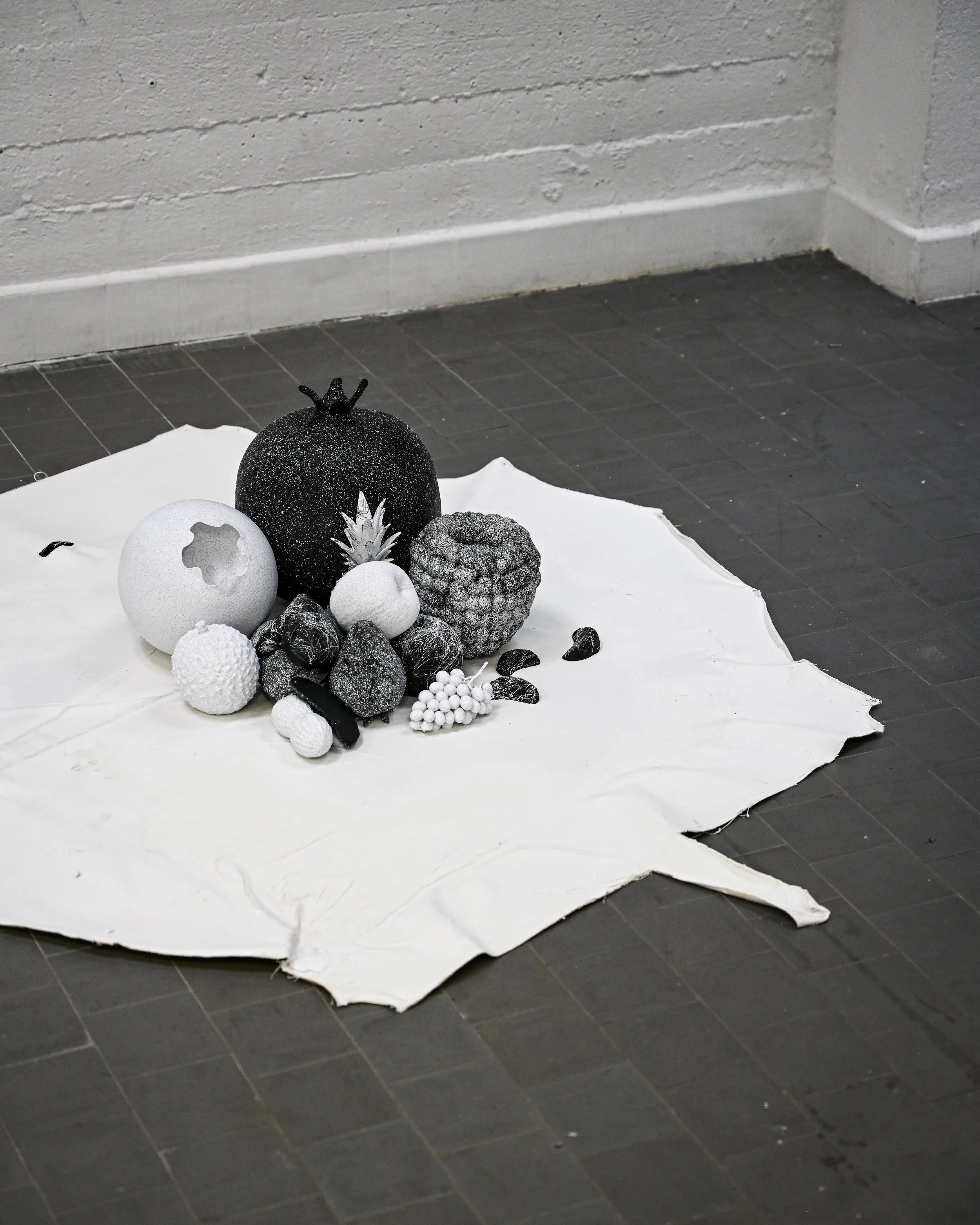 Decorative black and white sphere ornaments, a small pineapple figurine, and black and white textured objects are arranged on a white cloth on a dark tiled floor.